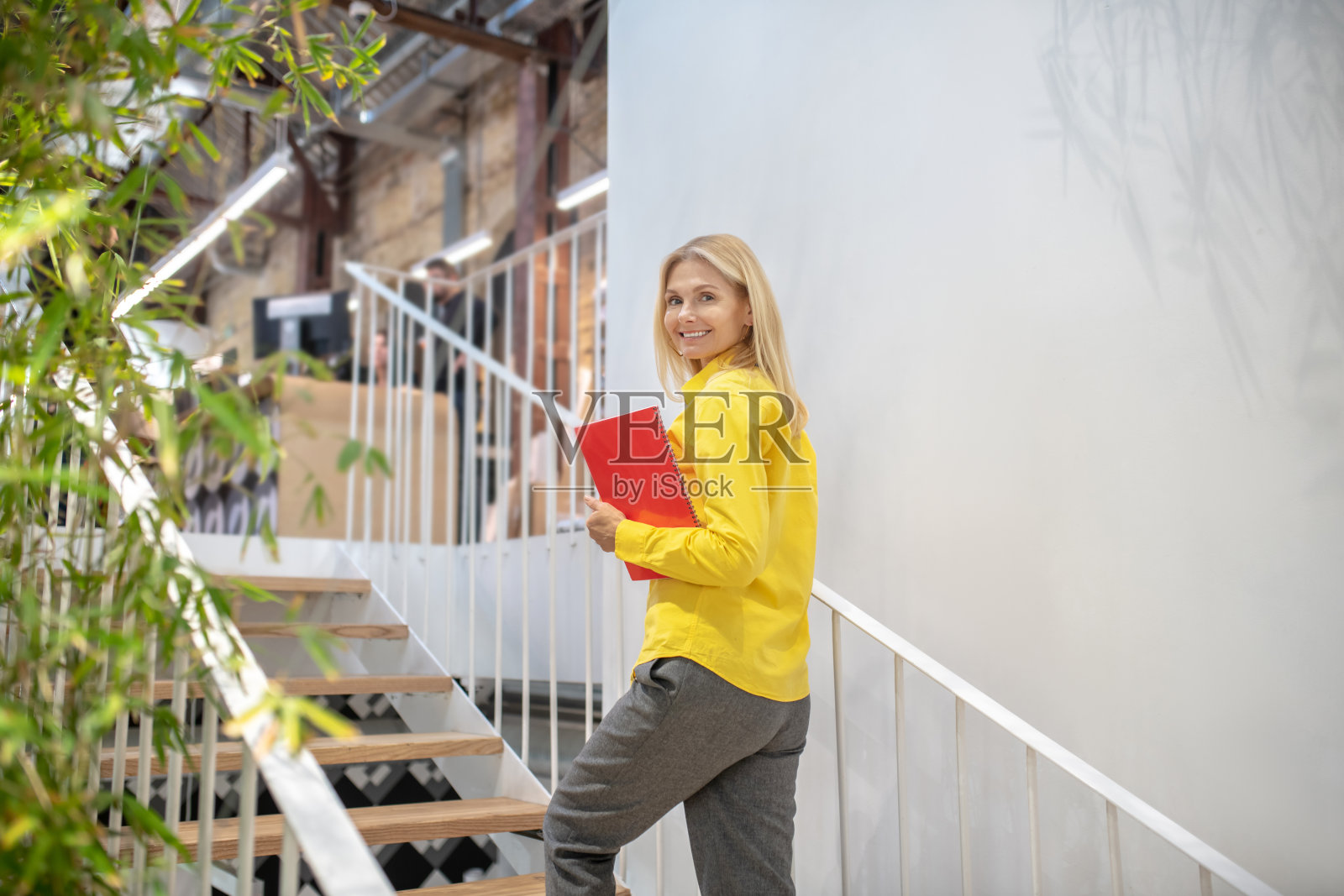 拿着红色笔记本爬楼梯的金发女人照片摄影图片