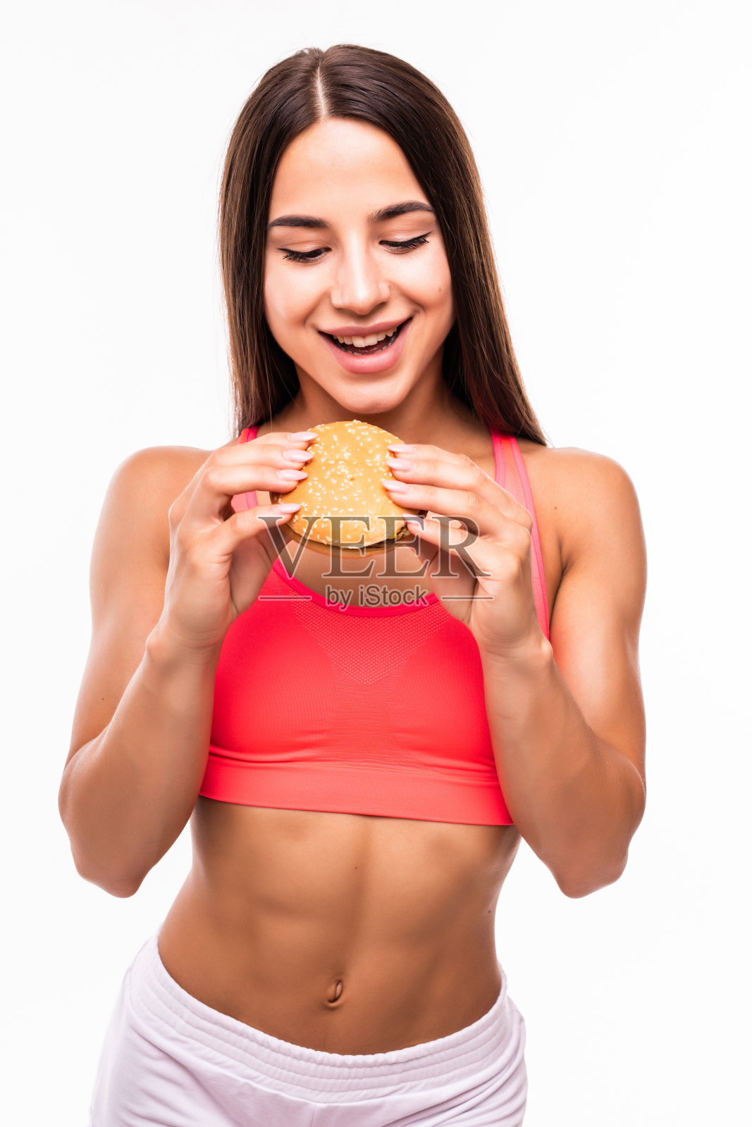 在白色背景下手拿汉堡的运动型女人。运动型女人吃不健康的食物照片摄影图片