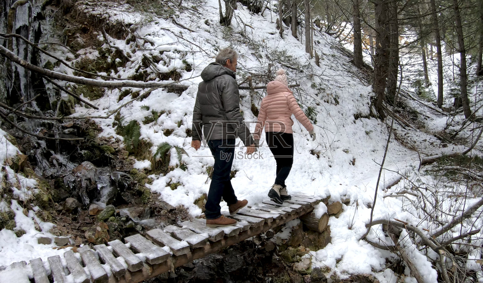 一对成年夫妇徒步穿越积雪覆盖的木板路照片摄影图片