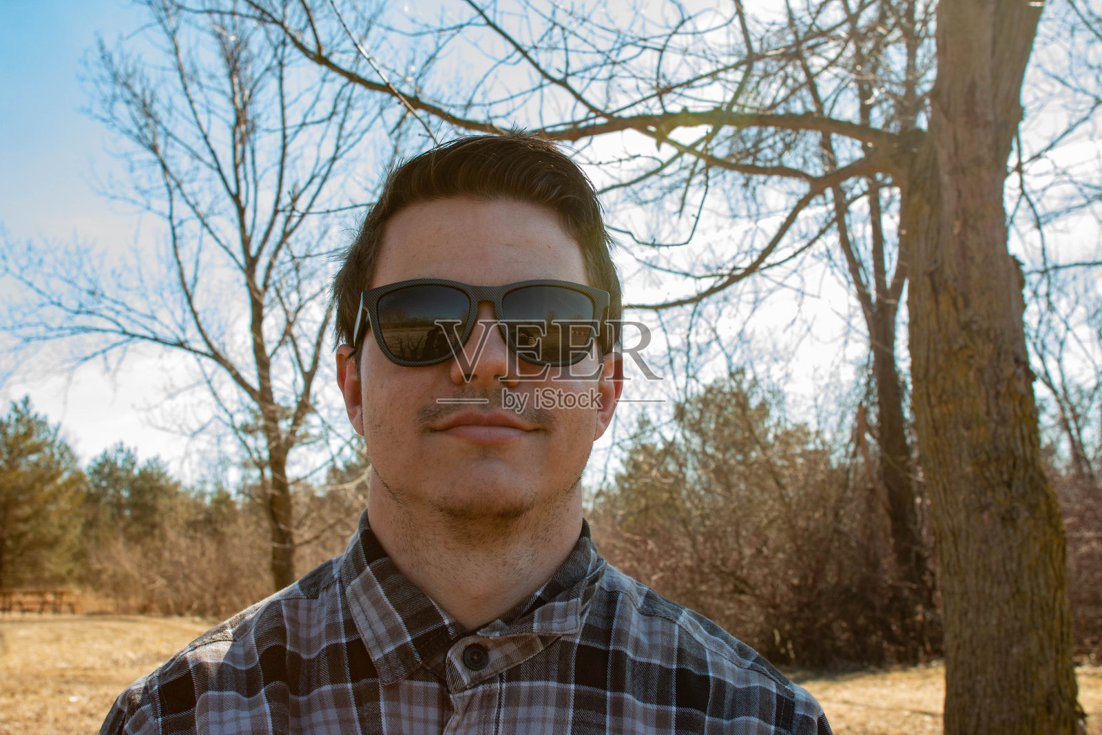 年轻人戴着太阳镜，穿着格子衬衫，坐在冬天的海滩上照片摄影图片