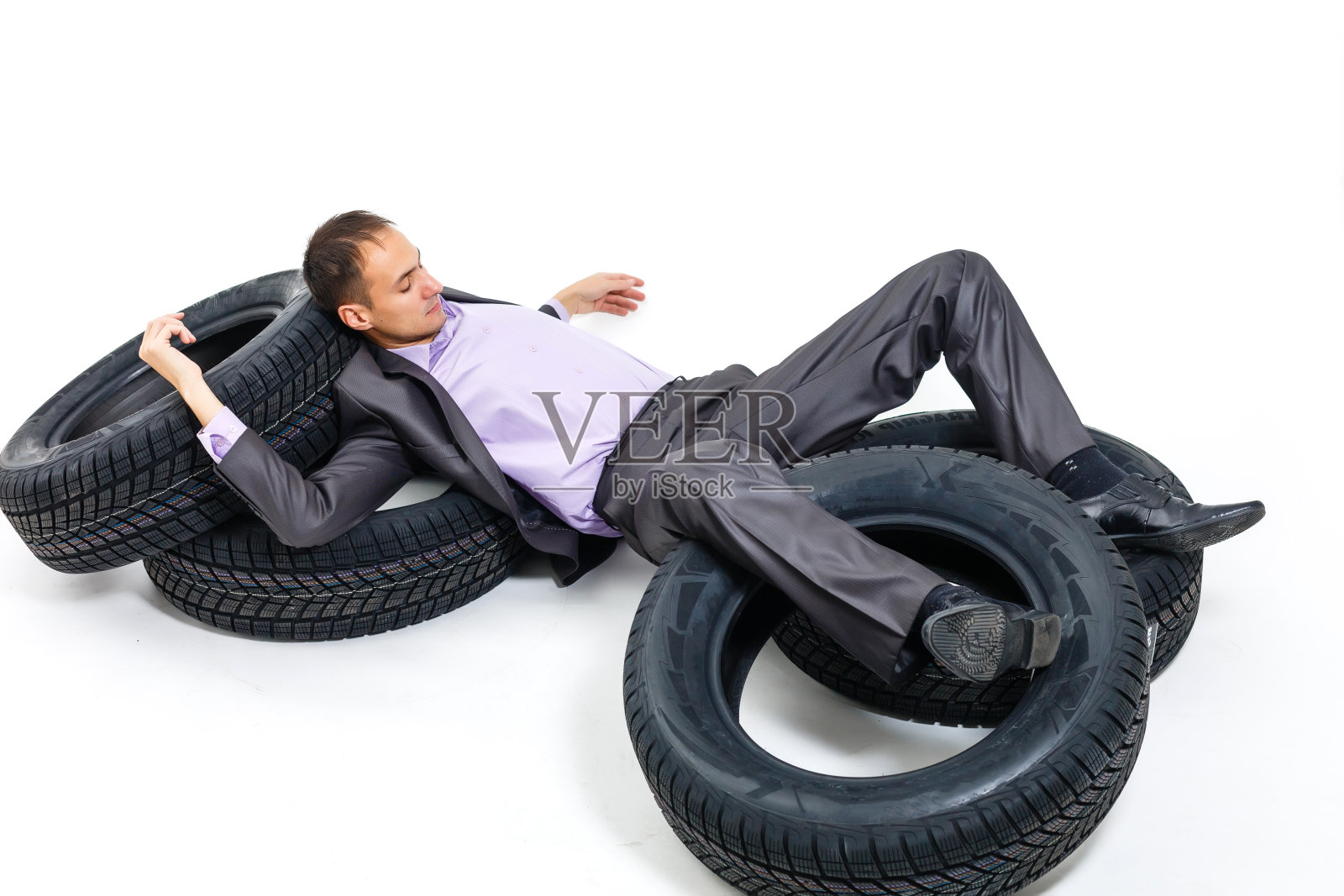 年轻商人倚靠在轮胎堆上的全身像照片摄影图片
