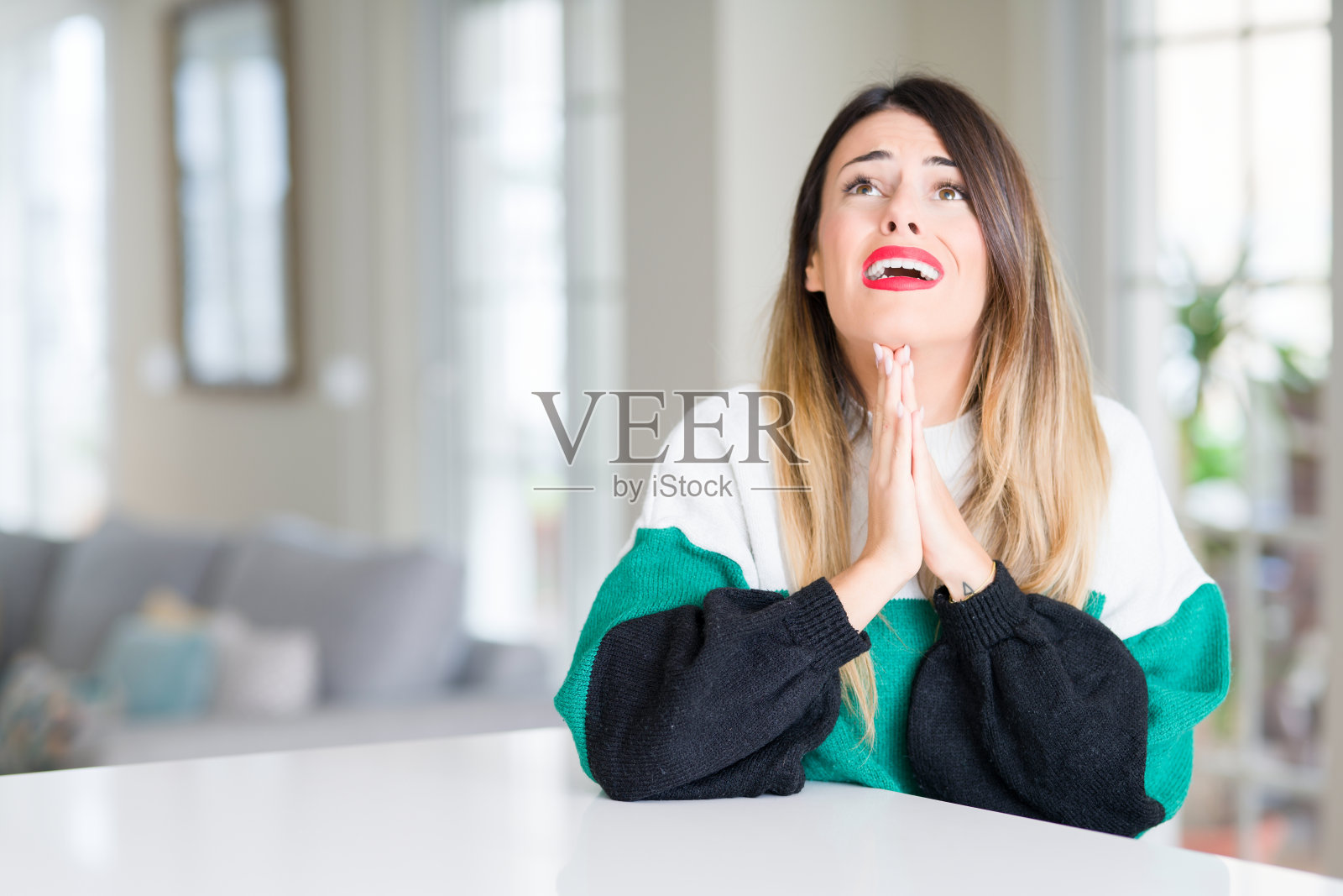 年轻漂亮的女子穿着冬衣在家乞讨祈祷，脸上带着希望的表情，非常情绪化和担忧。请求宽恕。宗教的概念。照片摄影图片