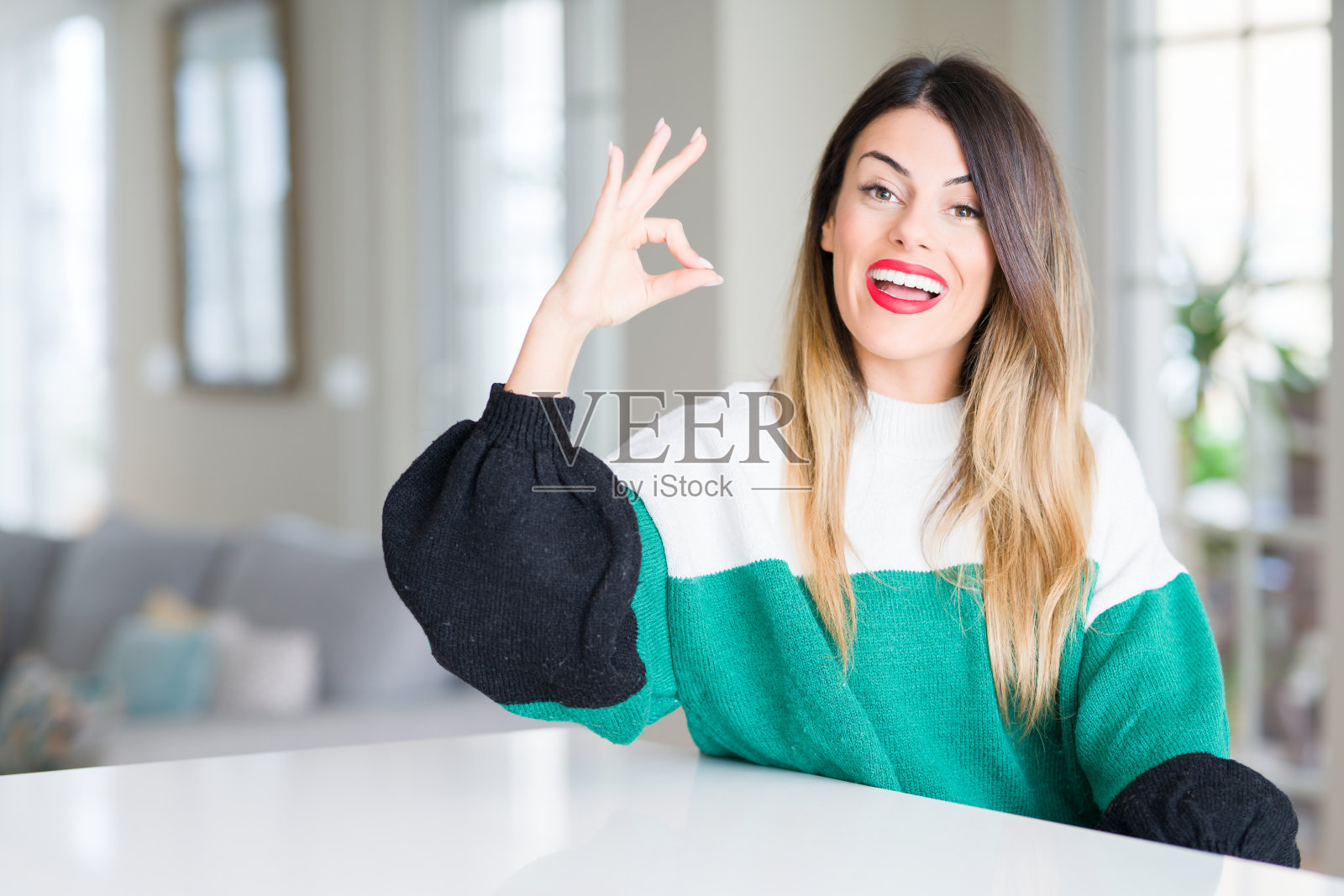 年轻漂亮的女人穿着冬天的毛衣在家里微笑积极做ok手势与手和手指。成功的表达。照片摄影图片