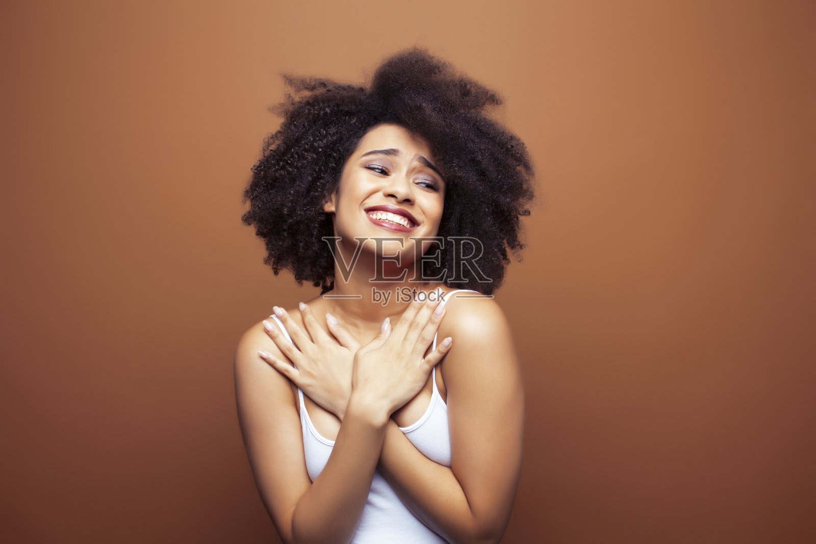 漂亮的年轻的非洲裔美国女人与卷曲的头发摆出愉快的手势在棕色的背景，生活方式的人的概念照片摄影图片