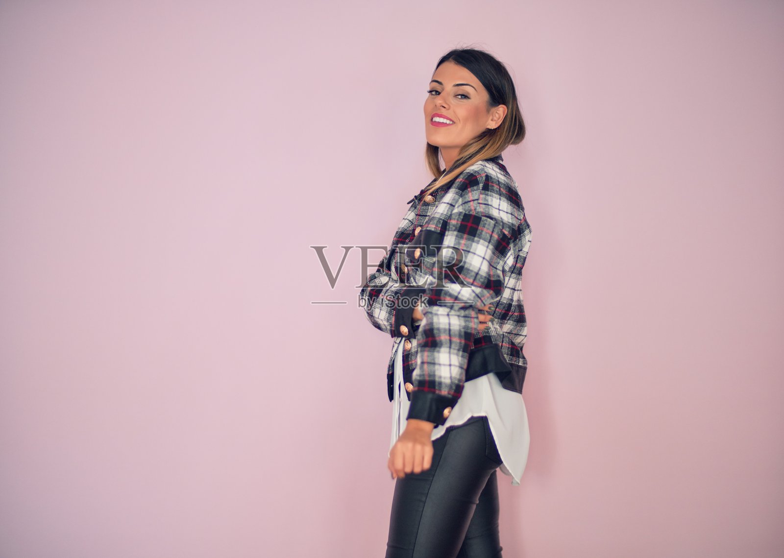 年轻漂亮的女人穿着时尚的衣服，微笑快乐和自信。站在孤立的粉红色背景上面带微笑照片摄影图片