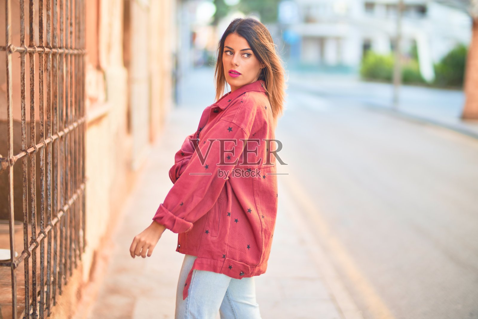 年轻漂亮的女人穿着红色夹克站在镇上的街道上照片摄影图片