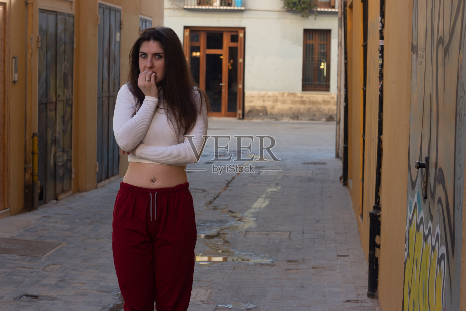 受惊吓的年轻女子感到恐惧，咬指甲，在城市里，白色上衣和红色裤子，黑暗的空气。将你的文本放在拷贝空间。照片摄影图片