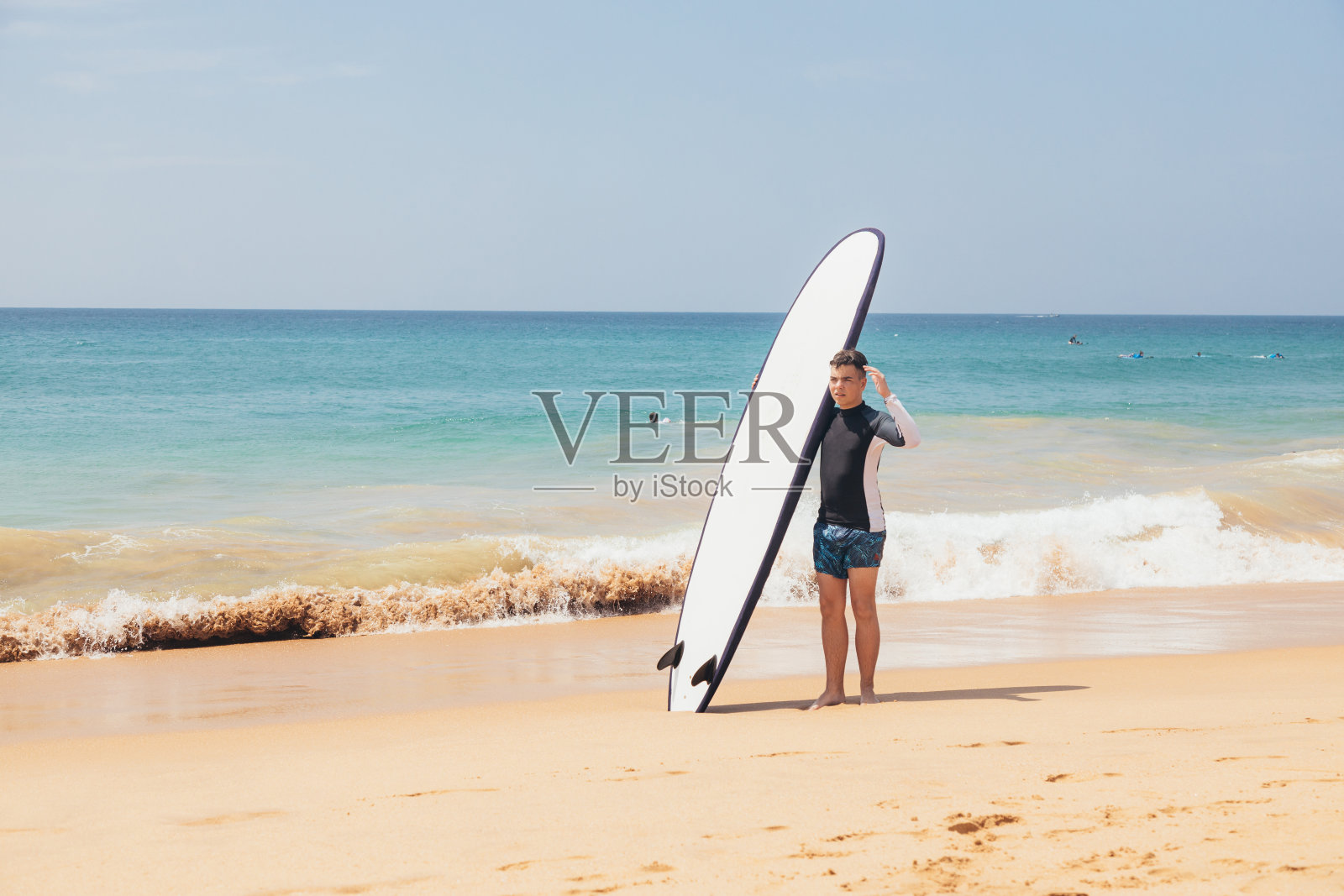 英俊的少年与冲浪板站在沙滩上的冲浪线。照片摄影图片