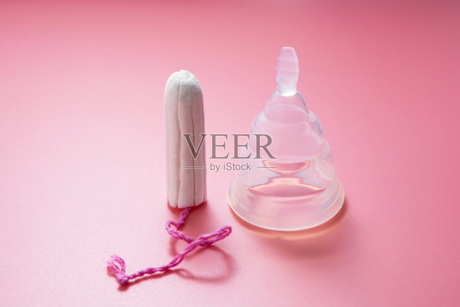 月经杯和女性卫生棉条，隔离在粉红色背景上。女性卫生产品。副本的空间。照片摄影图片