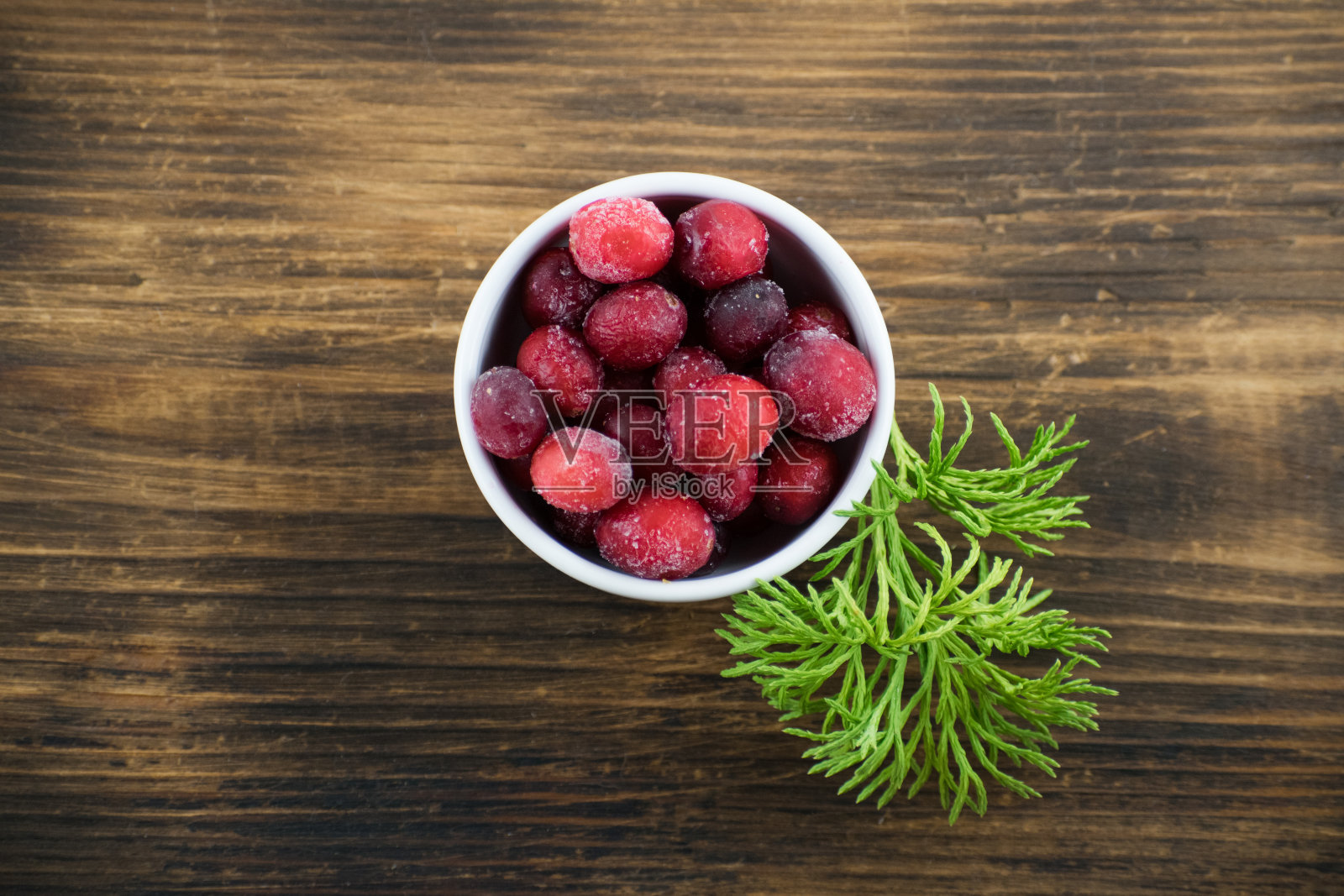 小红莓放在木板上的白碗里。小红莓冻结。白碗里装着蔓越莓和苔藓。照片摄影图片