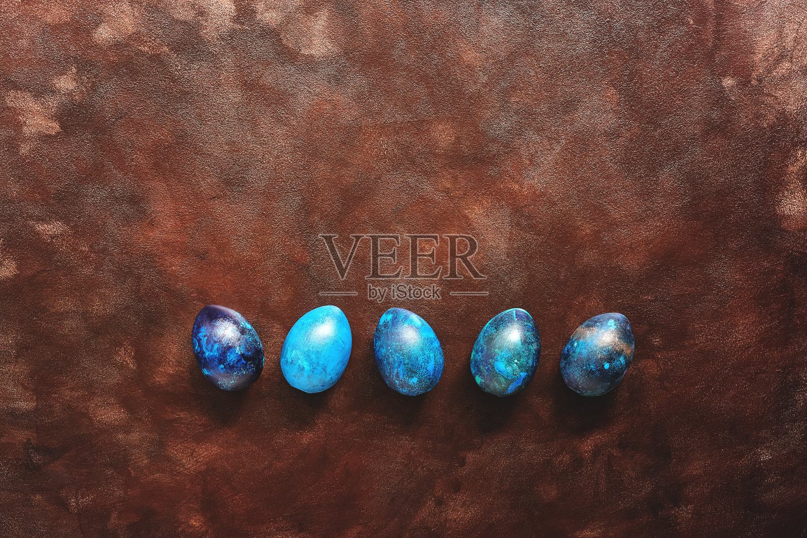 复活节装饰彩蛋排成一排，用蓝绿色涂在深棕色的背景、边框上。俯视图，平放。照片摄影图片