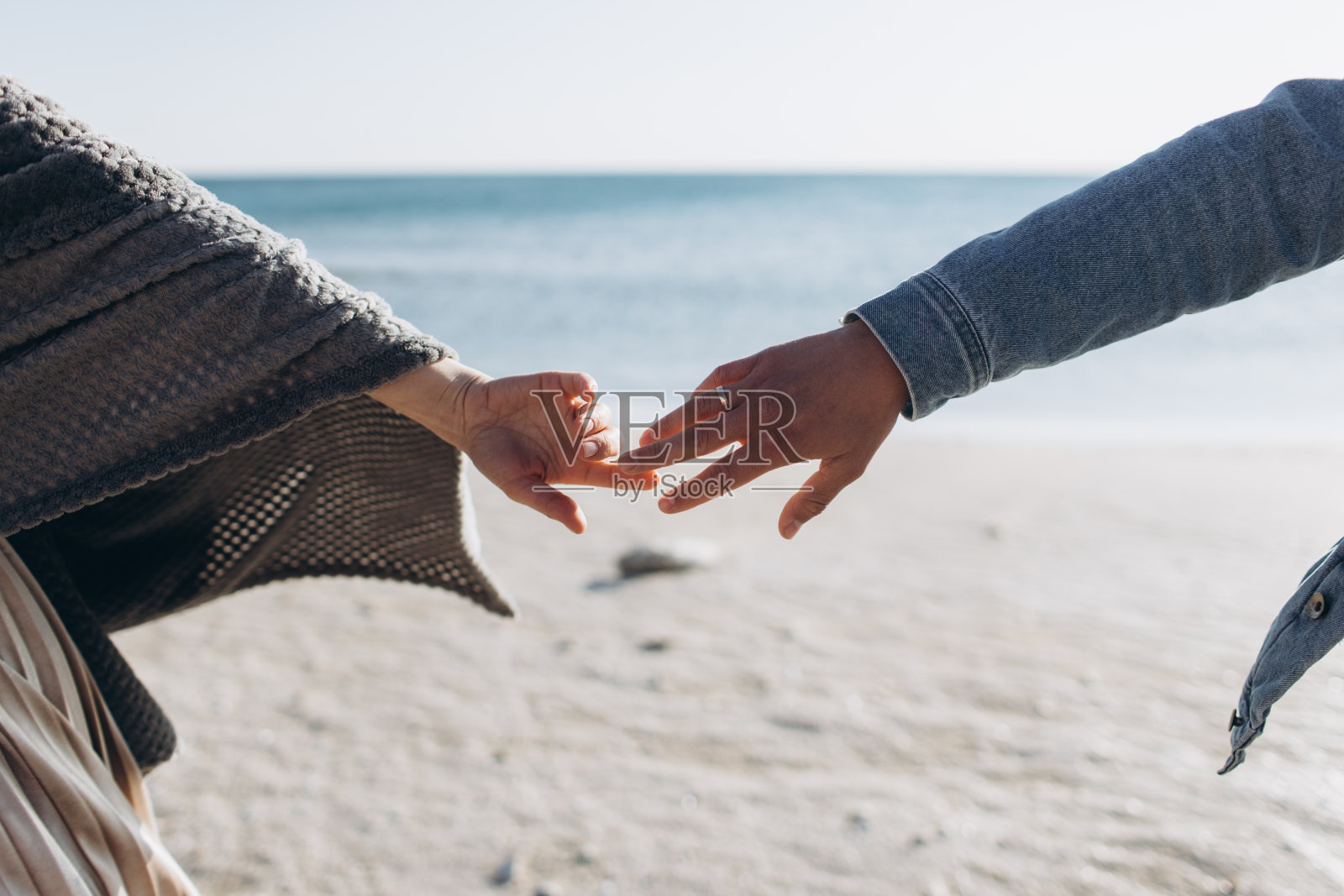 一对夫妇的手在大海的背景下互相伸展。照片摄影图片