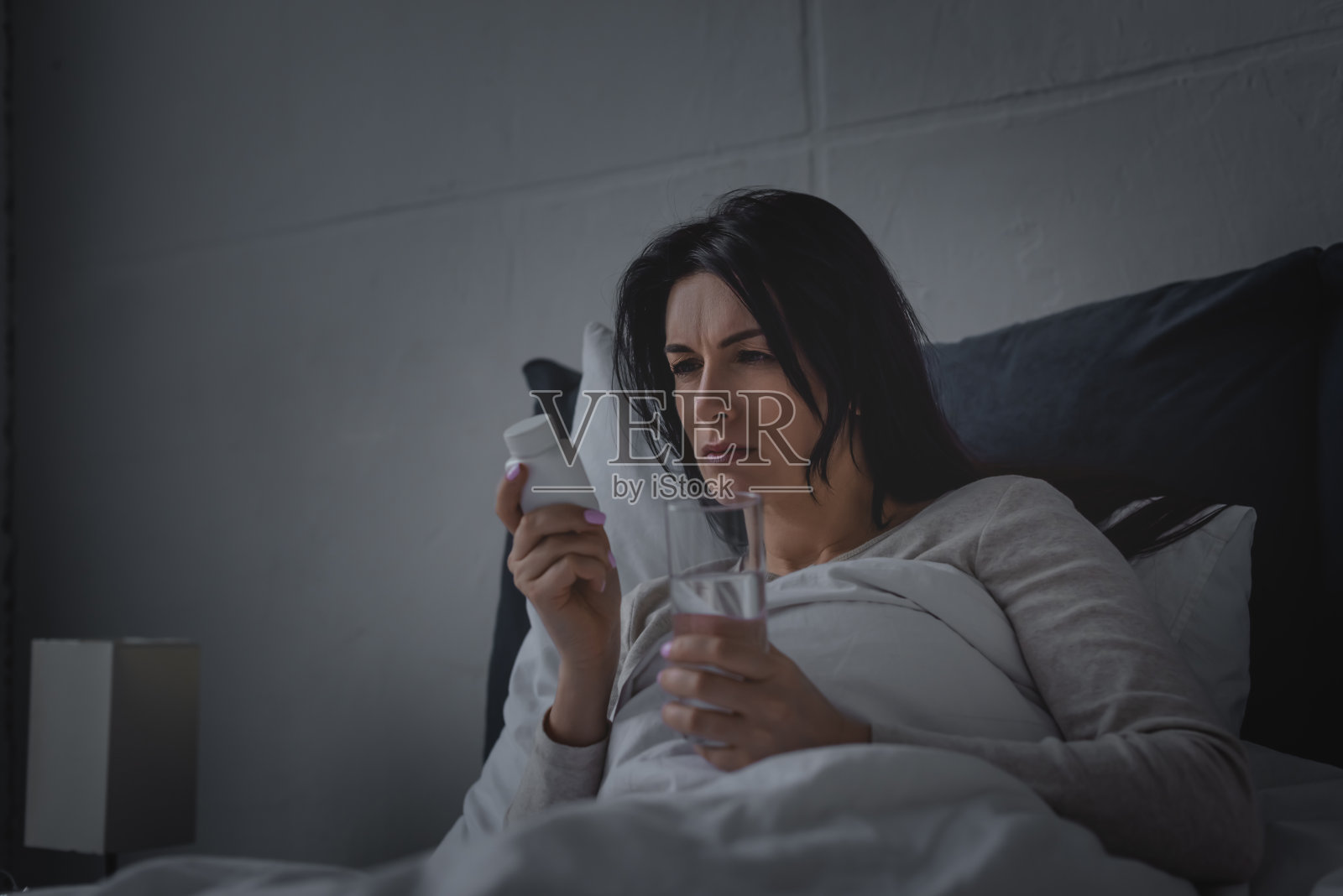 失眠的女人在卧室里拿着水杯和安眠药照片摄影图片