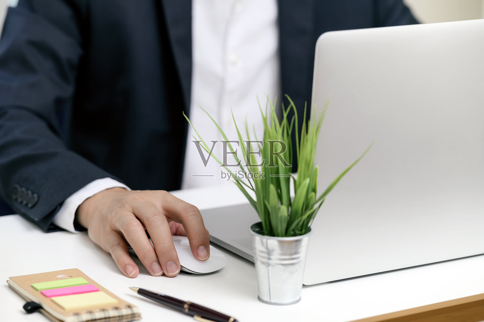 一名商人坐在办公桌前用鼠标操作笔记本电脑的镜头。照片摄影图片