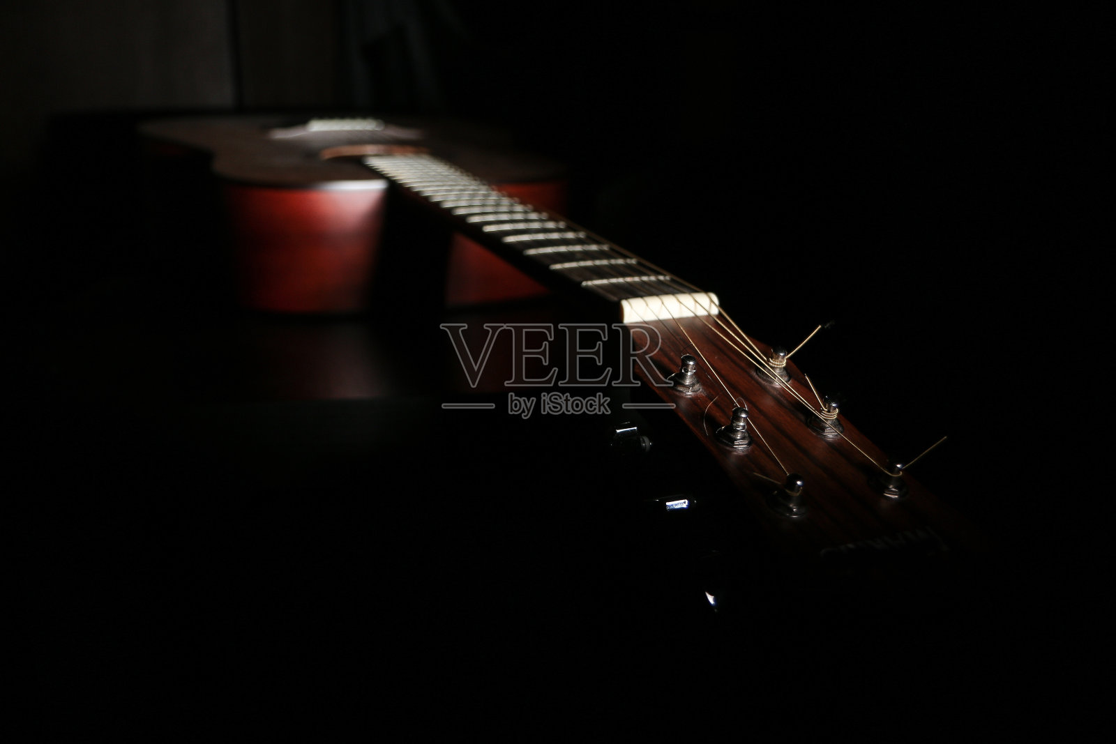 吉他的阴影图。它位于黑暗中，在少量光线下只有一部分可见。照片摄影图片