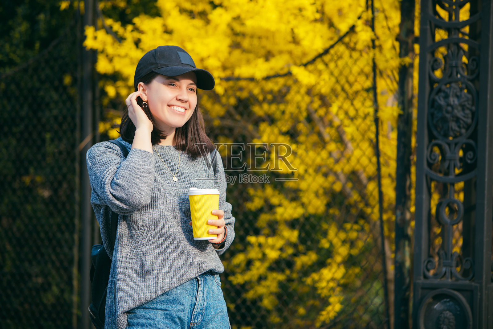 戴帽子的时尚年轻女子在户外用黄色纸杯喝咖啡照片摄影图片