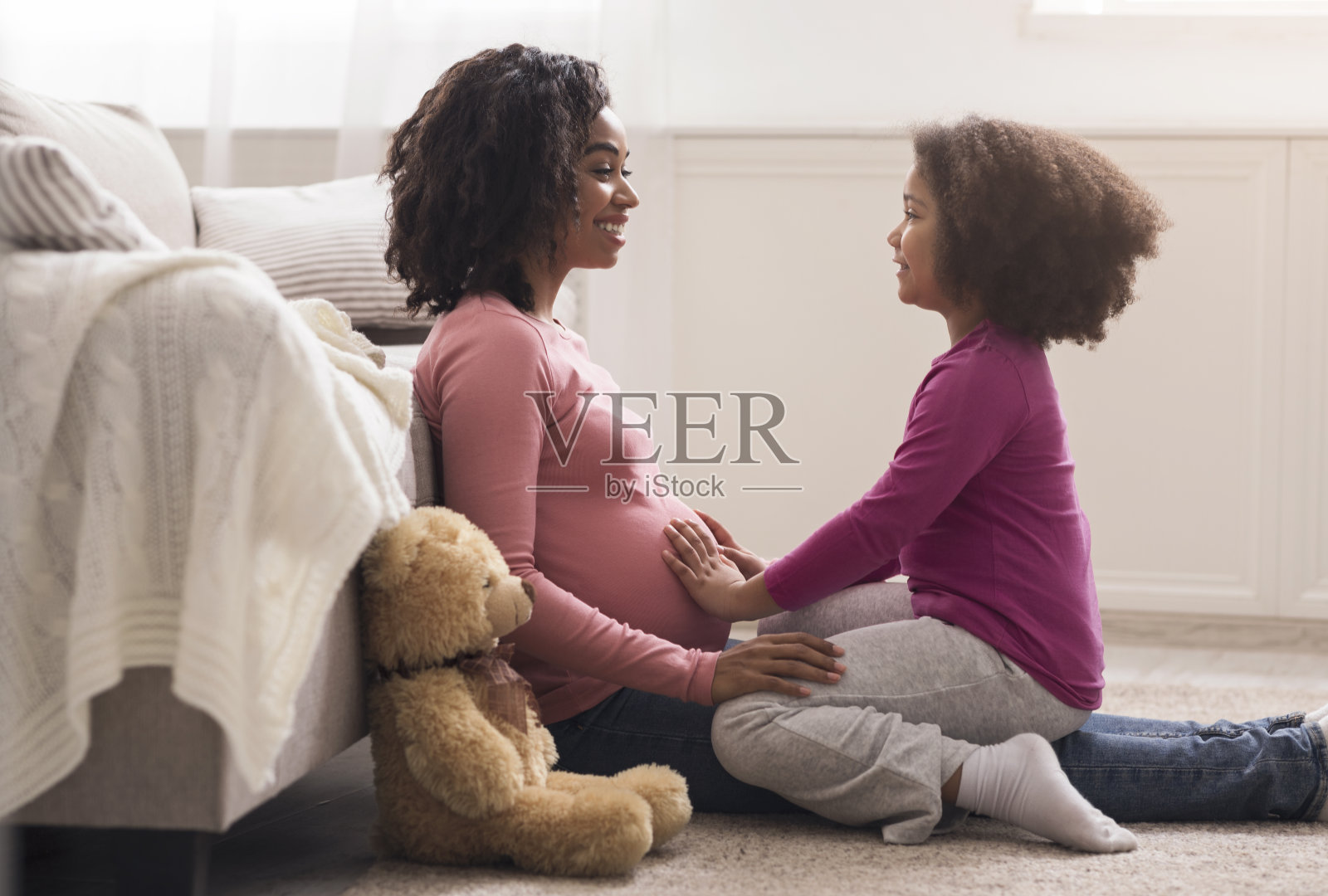 非洲裔小女孩摸着怀孕的妈妈的肚子，感觉宝宝在踢她照片摄影图片