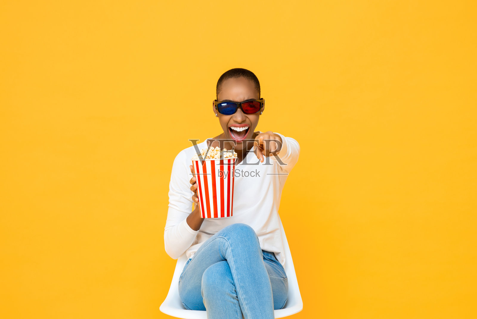 快乐的非裔美国妇女戴着3D眼镜和爆米花，在黄色演播室背景下笑着看电影照片摄影图片