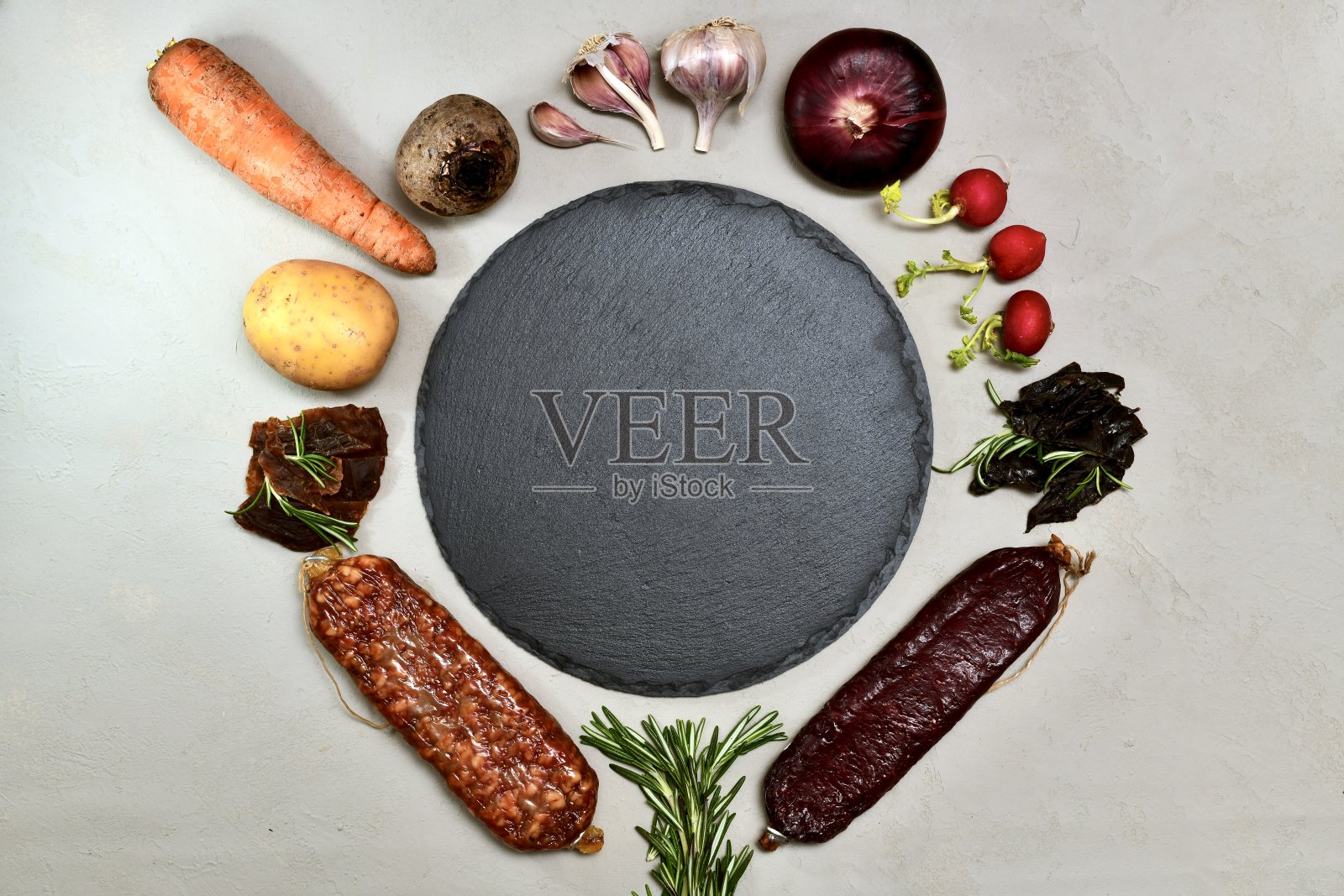 中间是一个黑色的圆形空底，周围是一圈干肉、蔬菜和熏香肠。照片摄影图片