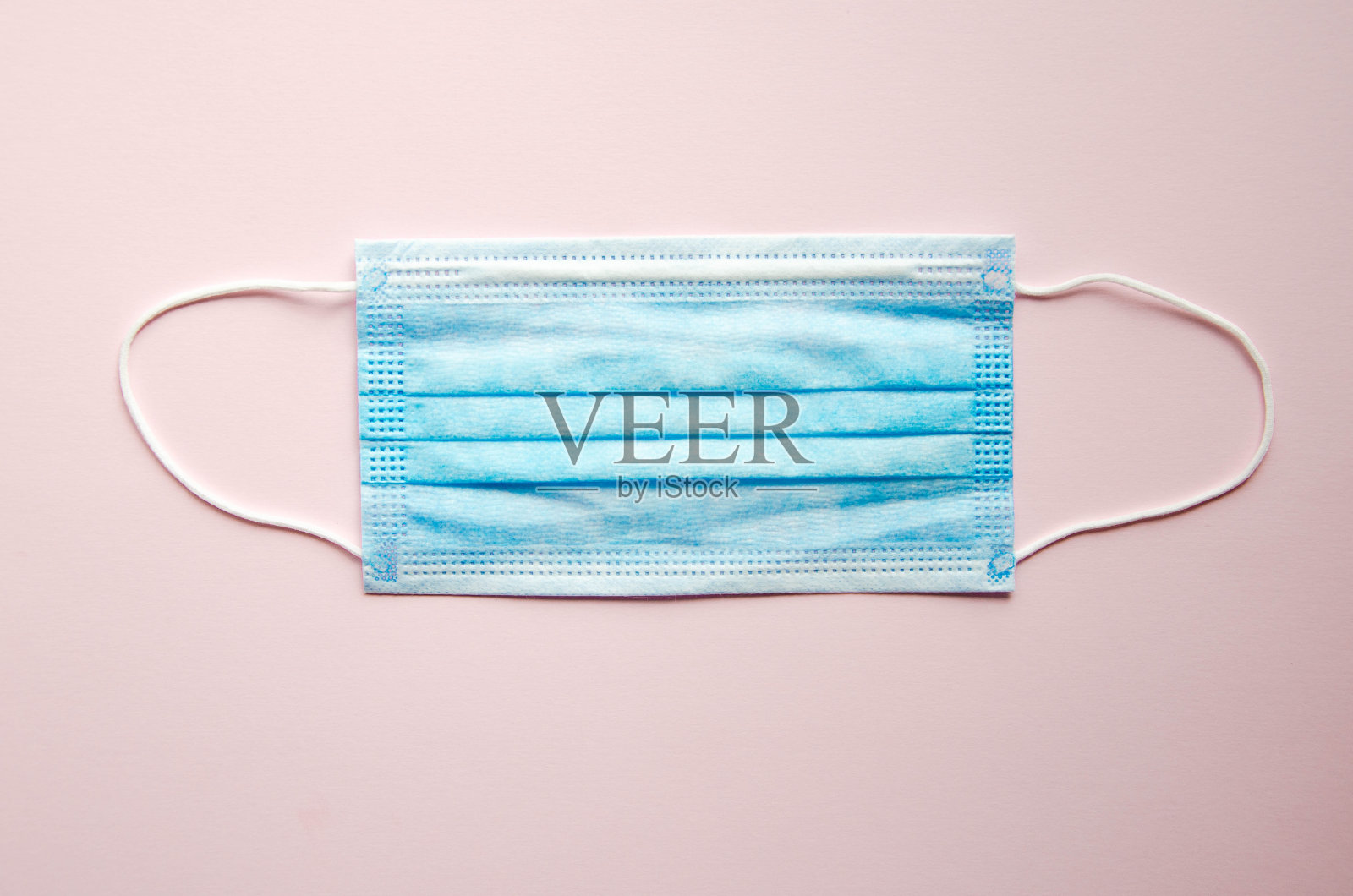 一个蓝色的医用口罩孤零零地躺在粉红色的背景上。文本。副本的空间。新型冠状病毒肺炎照片摄影图片