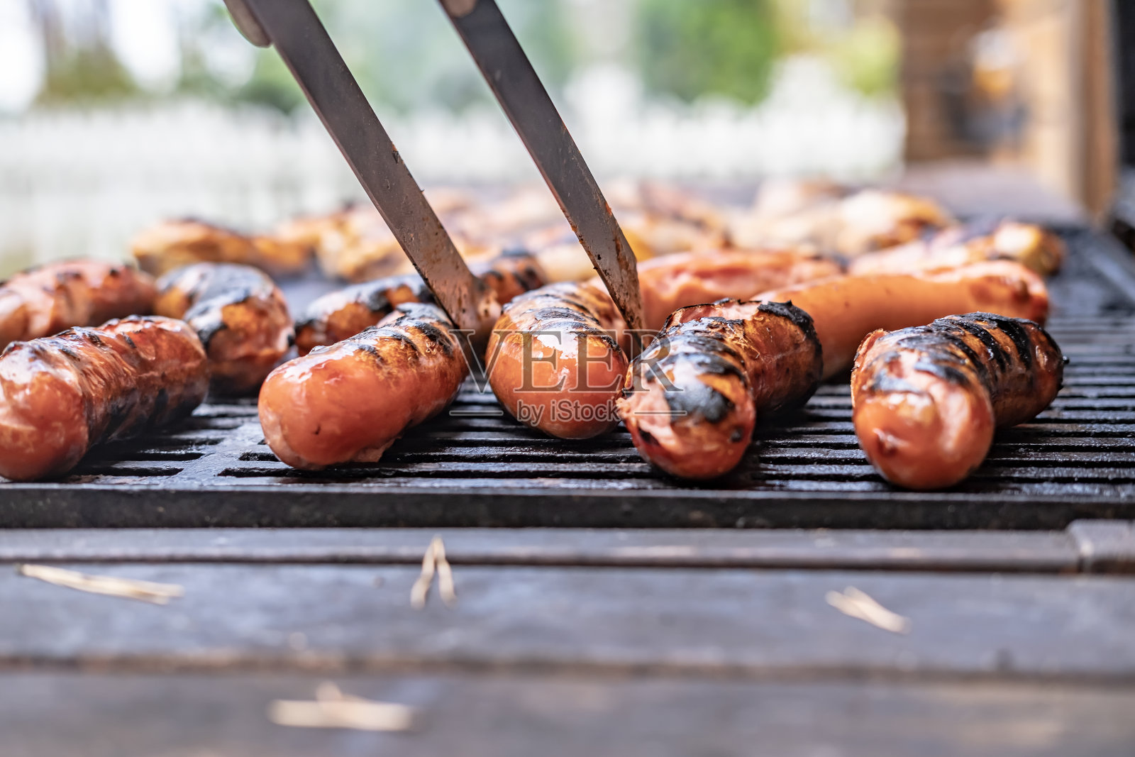 完成的香肠和烤鸡，从热格栅使用镊子。照片摄影图片