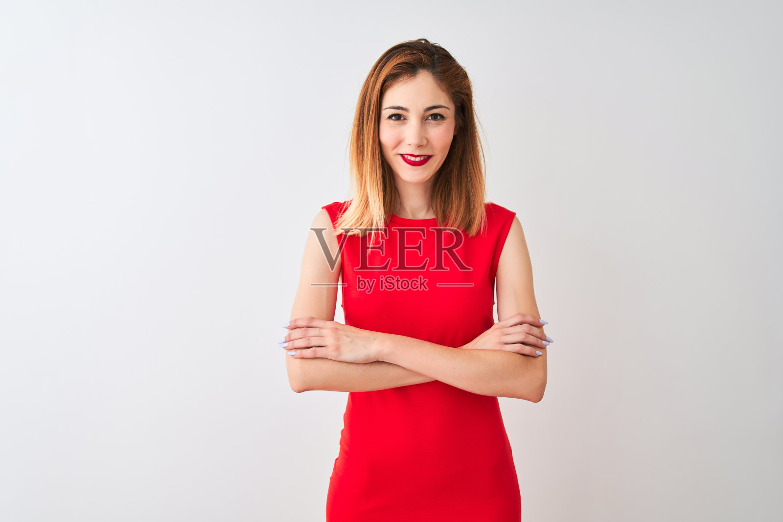 穿着优雅红裙的红发女商人站在孤立的白色背景前，面带幸福的微笑，双臂交叉看着镜头。积极的人。照片摄影图片