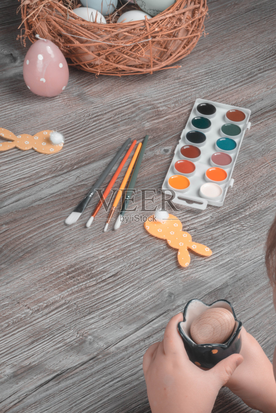 宝宝手翻复活节彩蛋。木制桌子上的颜料，画笔，兔子，窝照片摄影图片