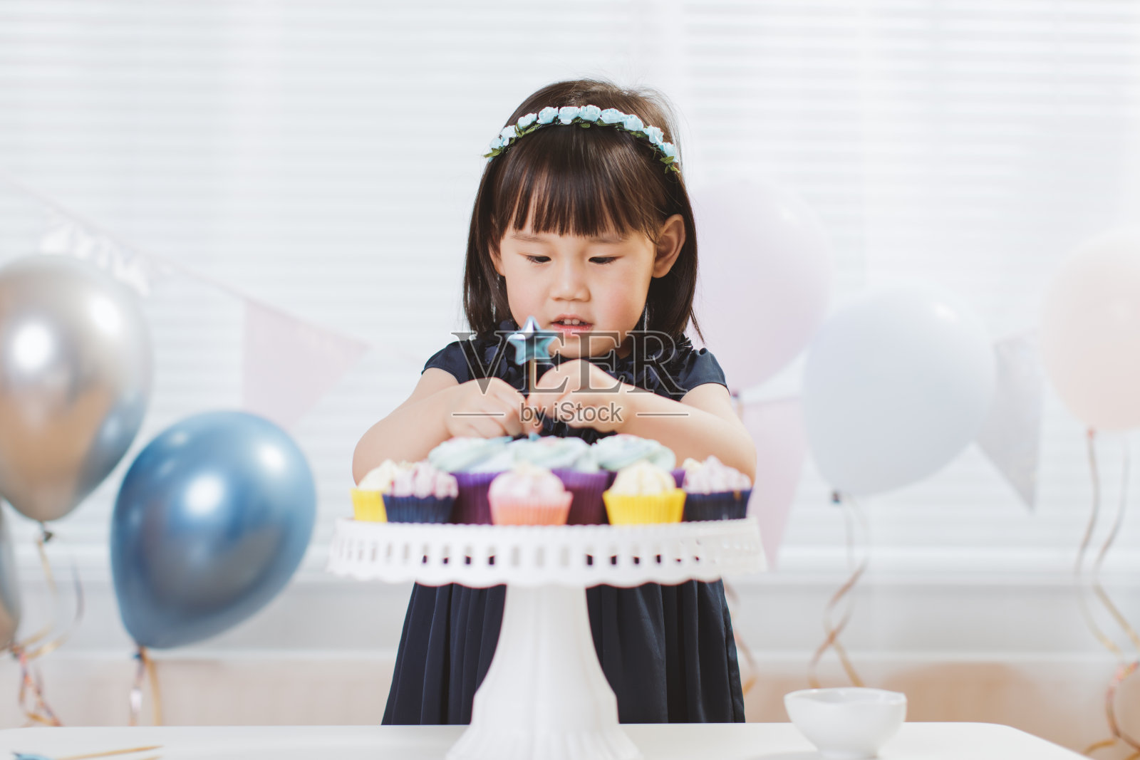 蹒跚学步的小女孩以窗户为背景装饰生日派对的纸杯蛋糕照片摄影图片