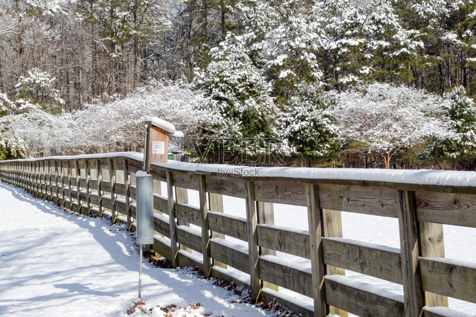 冬季暴风雪后，一个鸟类喂食器沿着当地公园的栅栏。照片摄影图片