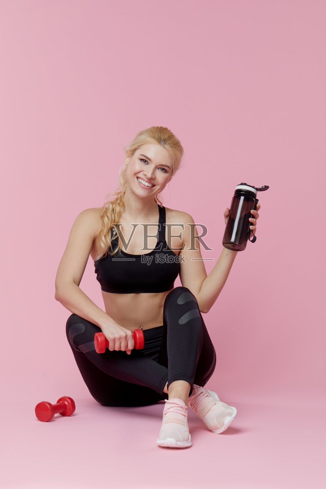 身材苗条的健身女孩在粉色背景上用哑铃训练肌肉照片摄影图片
