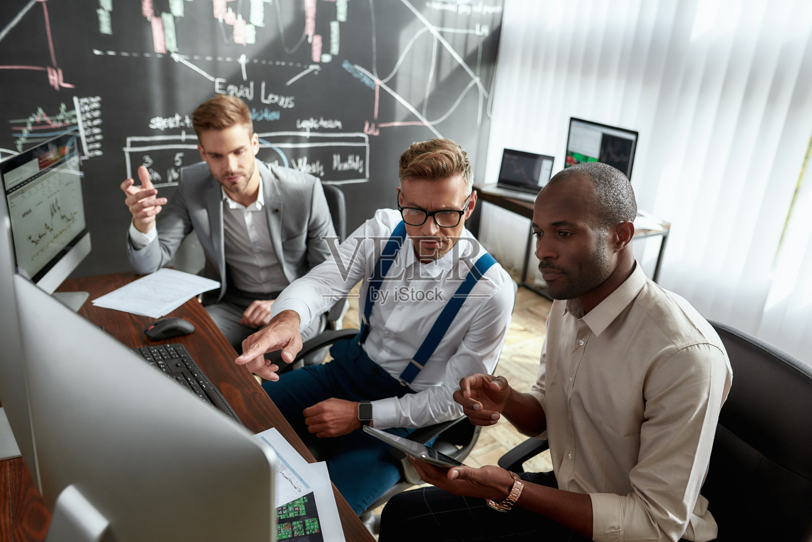 创建业务：交易员在办公室电脑前讨论策略照片摄影图片