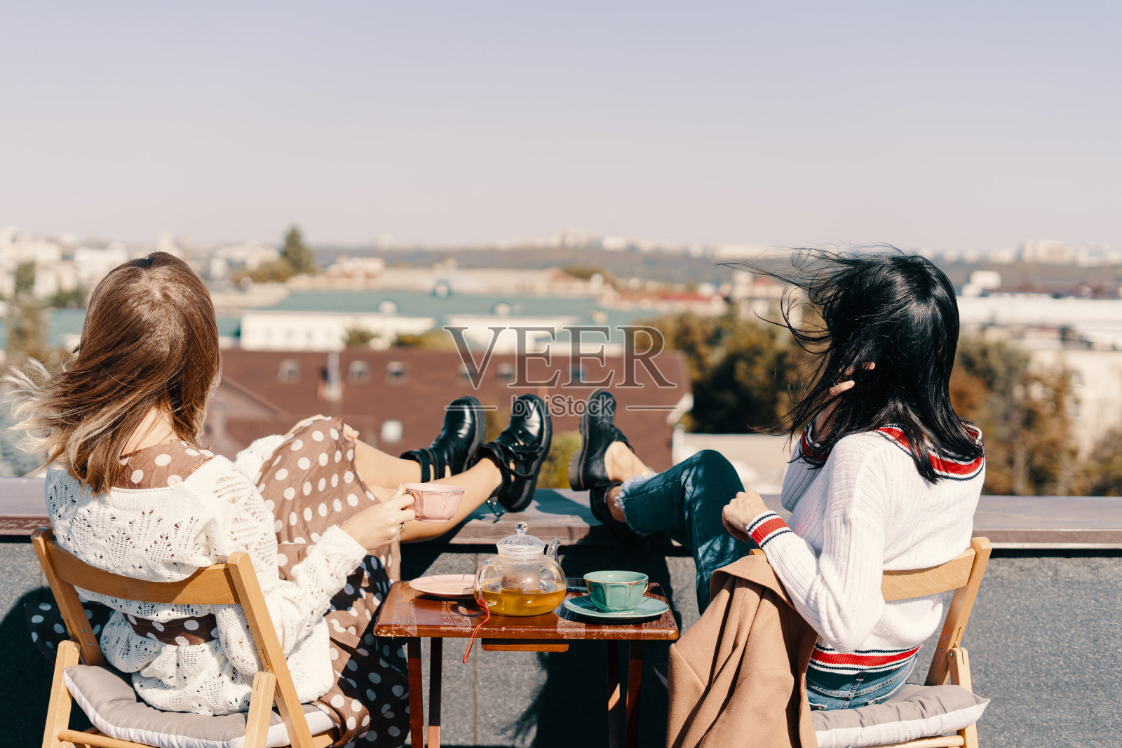 两个漂亮的女孩在屋顶上俯瞰城市，享受茶话会照片摄影图片