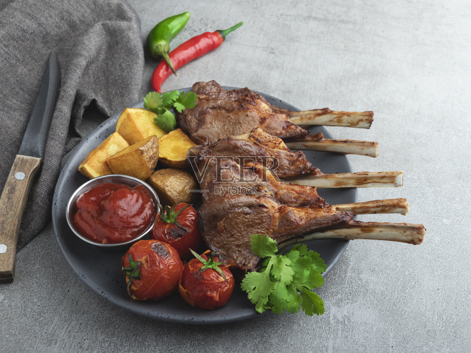 烤羊排放在木板上，配上红酱、土豆和西红柿照片摄影图片