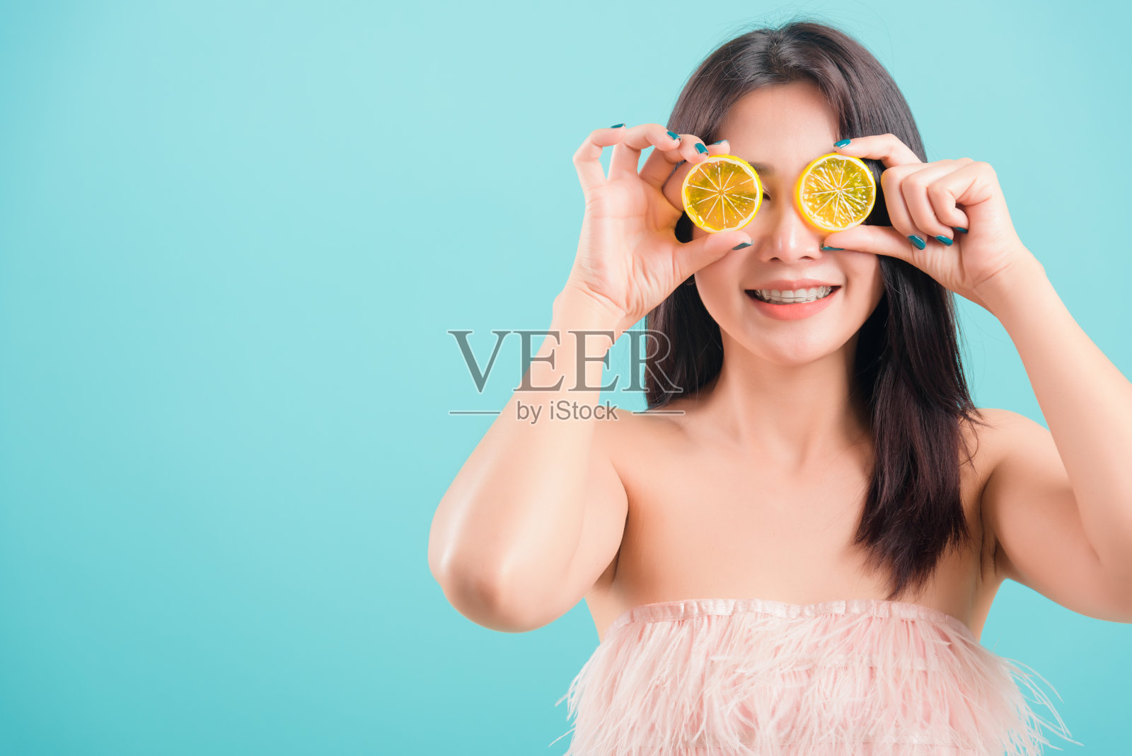 亚洲幸福的肖像美丽的年轻女子站在微笑拿一片橙色在她的眼睛前面的蓝色背景与文本复制空间照片摄影图片