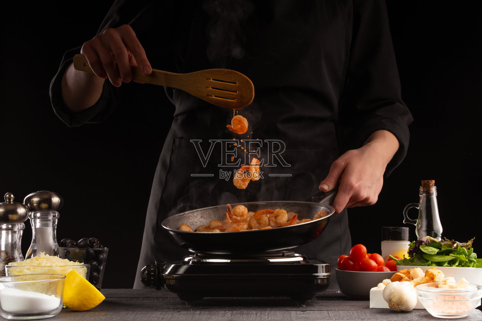 厨师用平底锅烹饪海鲜、虾和蔬菜。冻结。在黑色的背景上。照片摄影图片