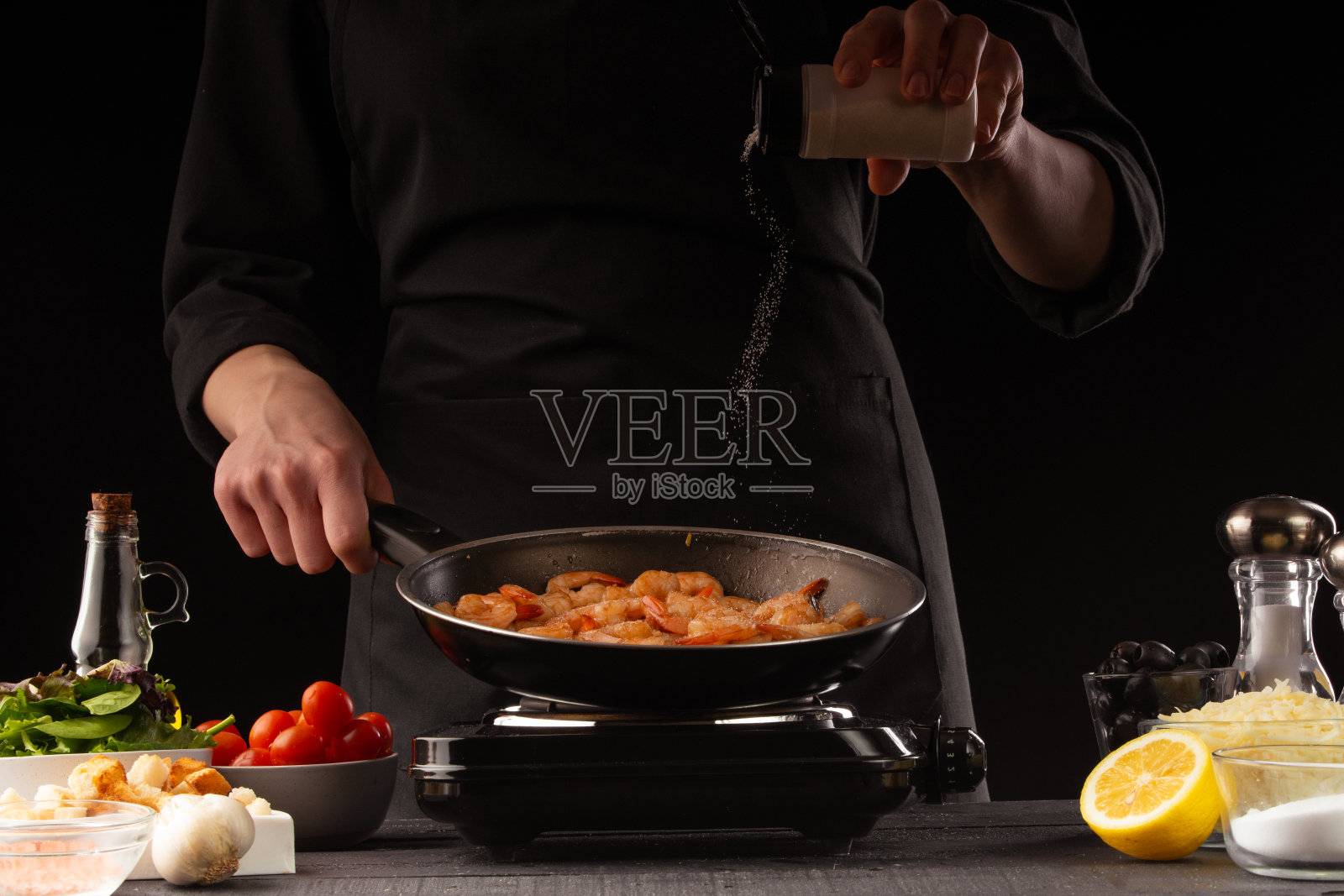厨师将海鲜、虾，撒上调味料，放在平底锅中，动态冷冻。以蔬菜为背景。黑色背景，烹饪和食谱，烹饪和健康饮食。照片摄影图片