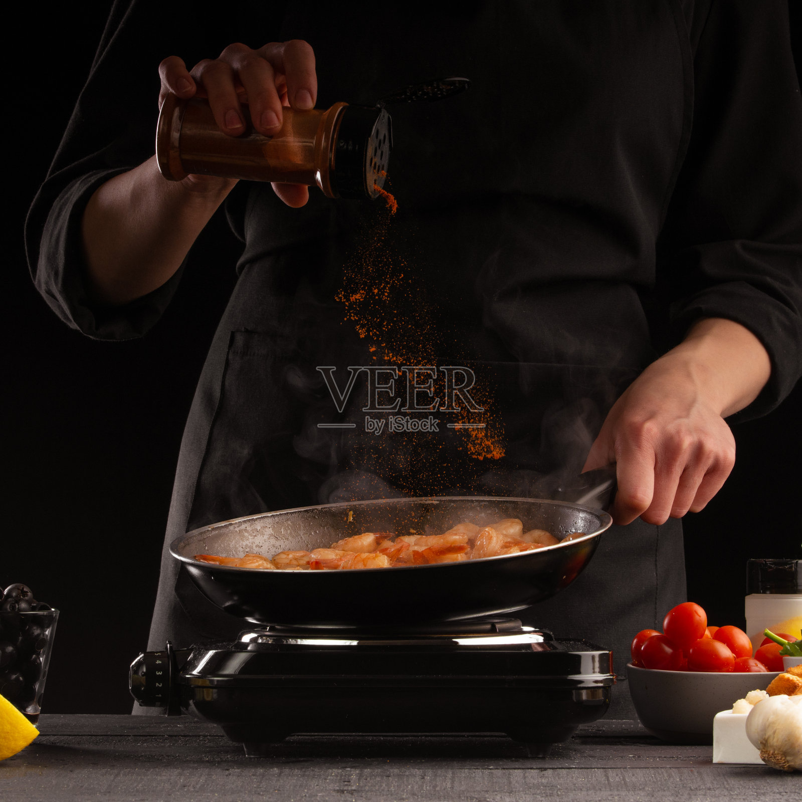 厨师将海鲜、虾，撒上调味料，放在平底锅中，动态冷冻。以蔬菜为背景。黑色背景，烹饪和食谱，烹饪和健康饮食。照片摄影图片