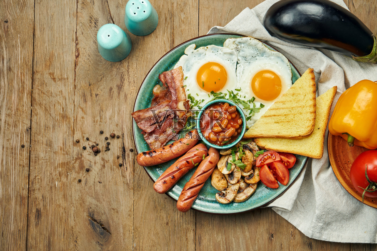 经典的英式早餐:吐司，熏香肠，培根，煎蛋，豆类和煎吐司放在一个蓝色的盘子里。顶视图,水平。木制背景照片摄影图片