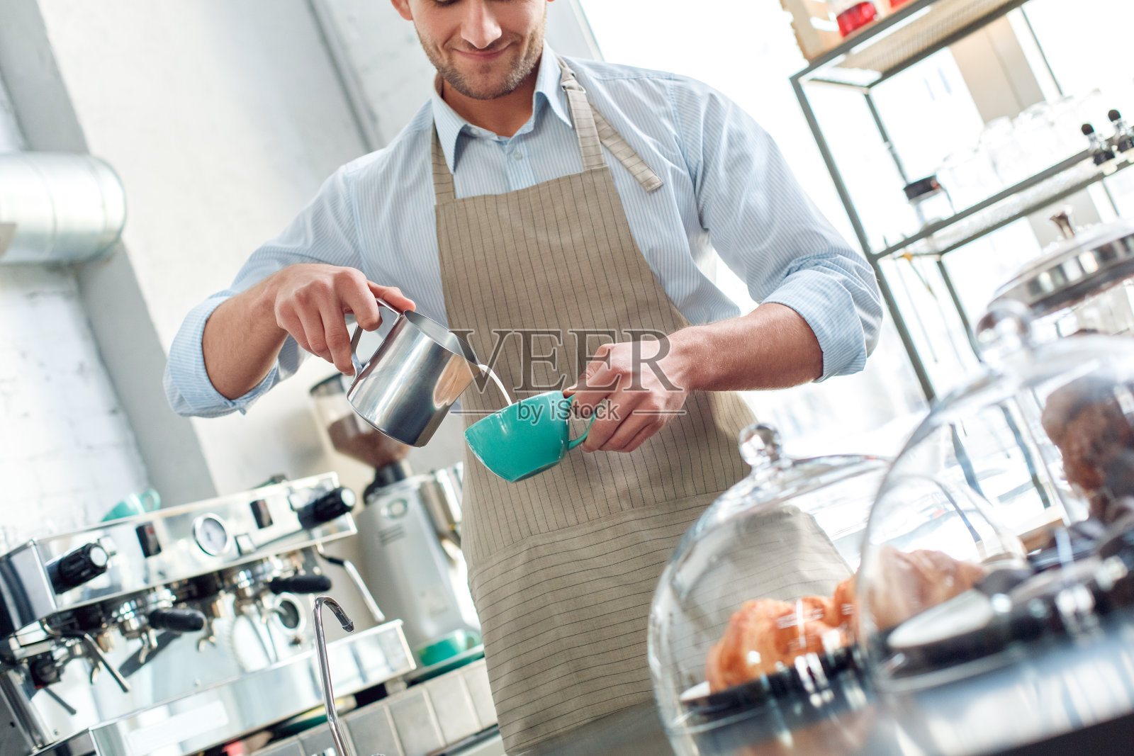 在餐厅工作的年轻的成年咖啡师，将搅打的牛奶和咖啡倒入杯中照片摄影图片