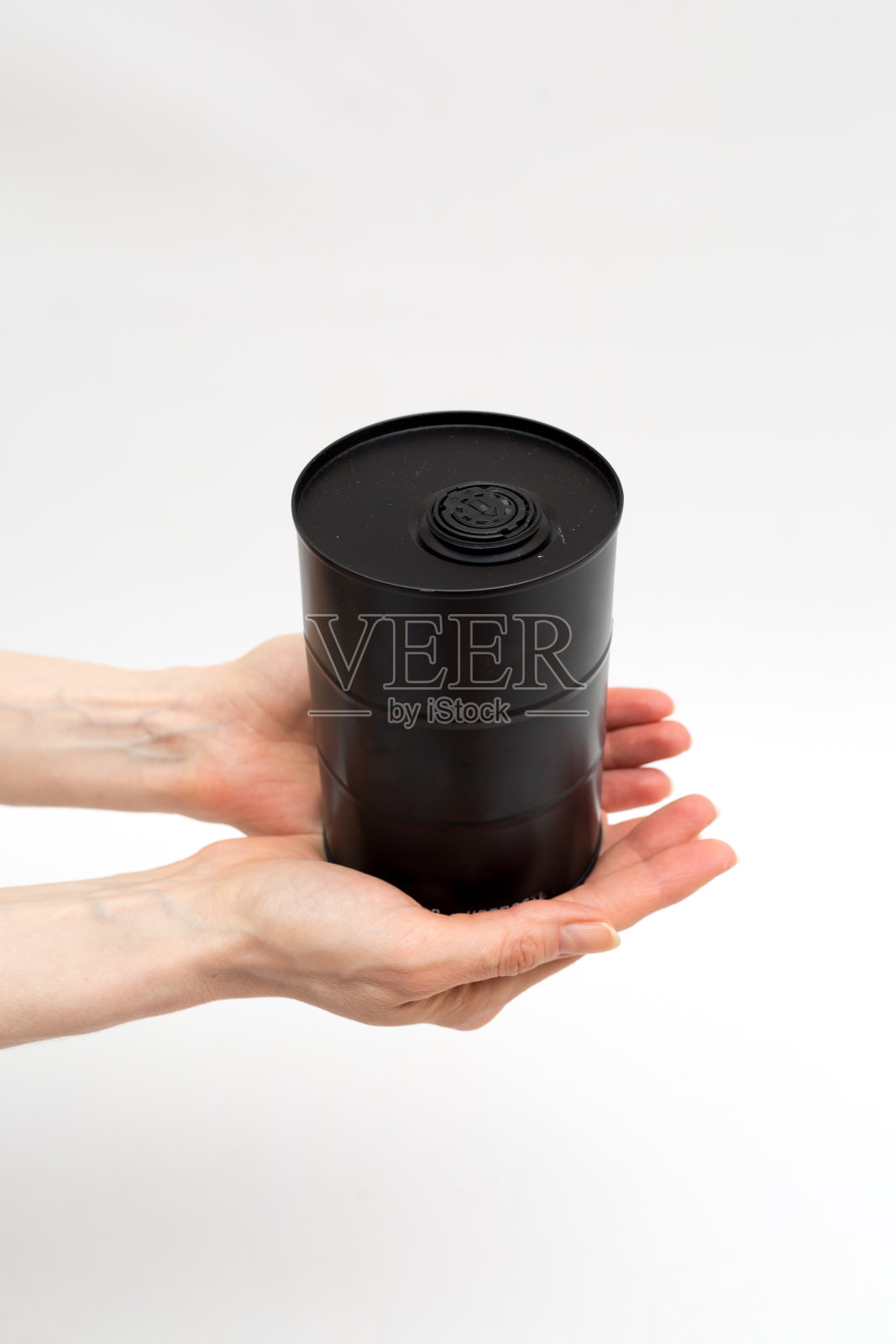 在白色的背景下，女性的手拿着一桶黑色的油。生态和环境。石油污染问题。石油危机，油价下跌照片摄影图片