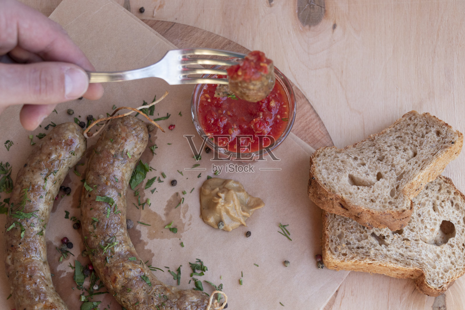 自制的纸香肠配上芥末和番茄酱。餐具和面包。俯视图上的一个木制背景。手拿着餐具。照片摄影图片