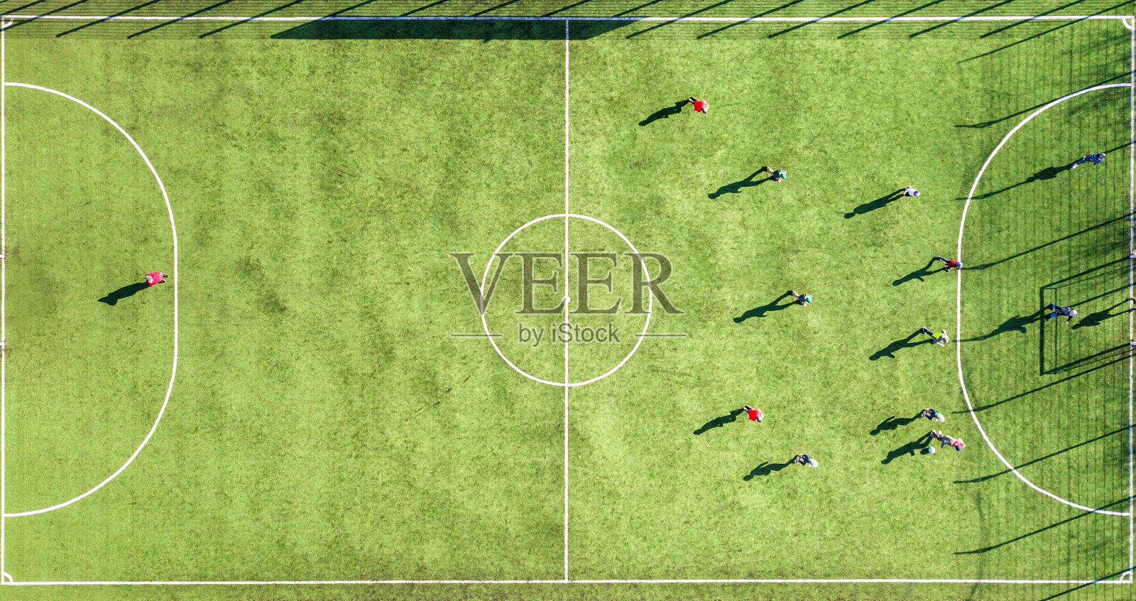 从上到下鸟瞰绿色足球场和球员踢足球。无人机拍摄的图像，小运动员在草地覆盖的体育场体育活动期间。照片摄影图片