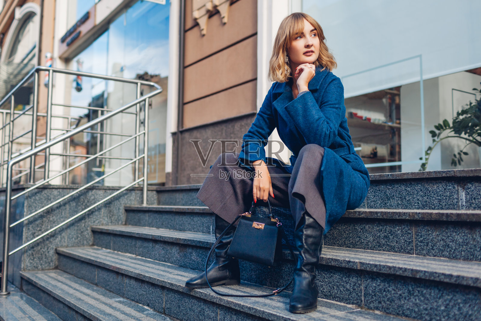 穿着蓝色外套带着钱包走在户外的时尚年轻女子的肖像。春季时尚女装配饰照片摄影图片