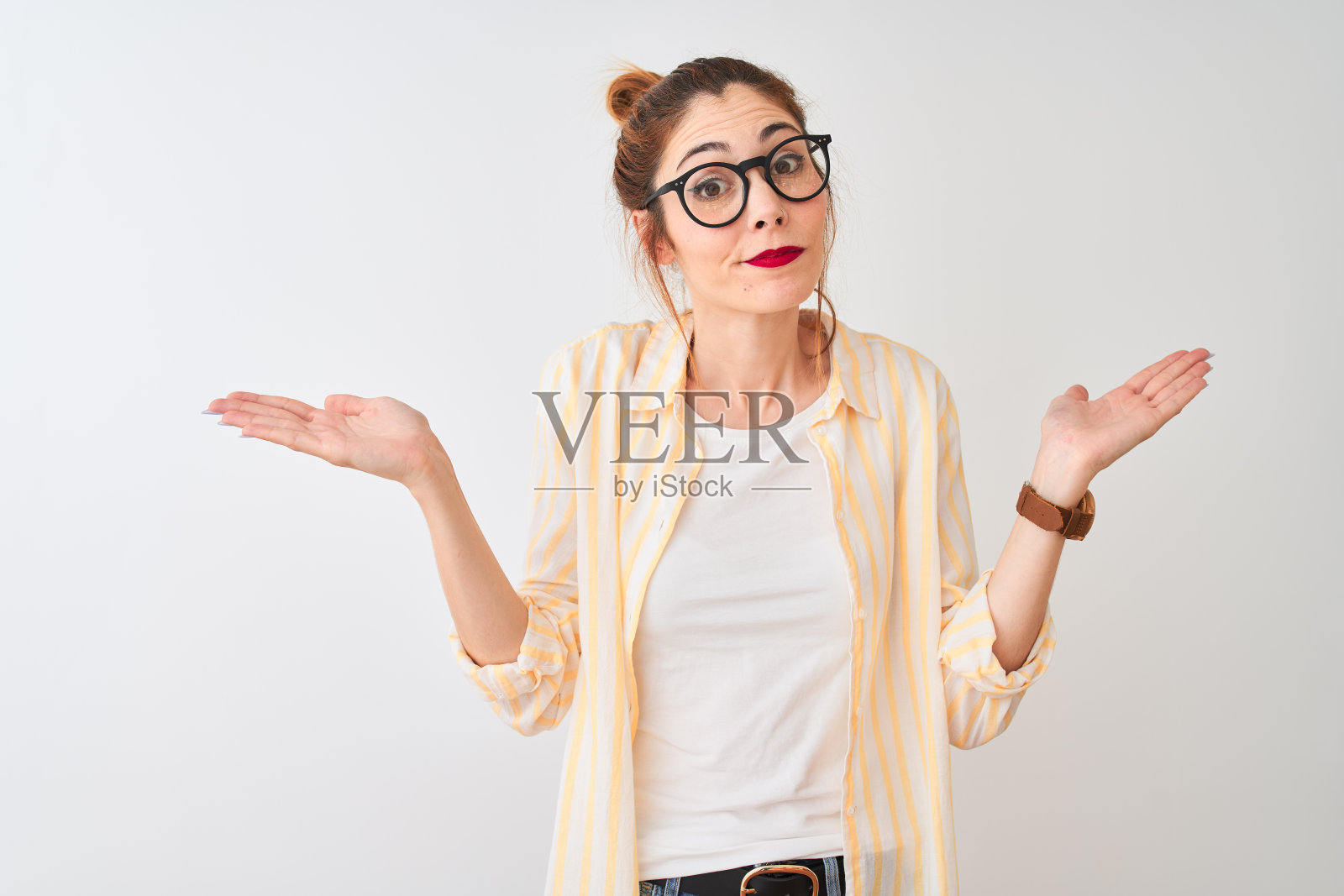 红发女人穿着条纹衬衫和眼镜，在白色背景前茫然无措，举手表示疑惑照片摄影图片