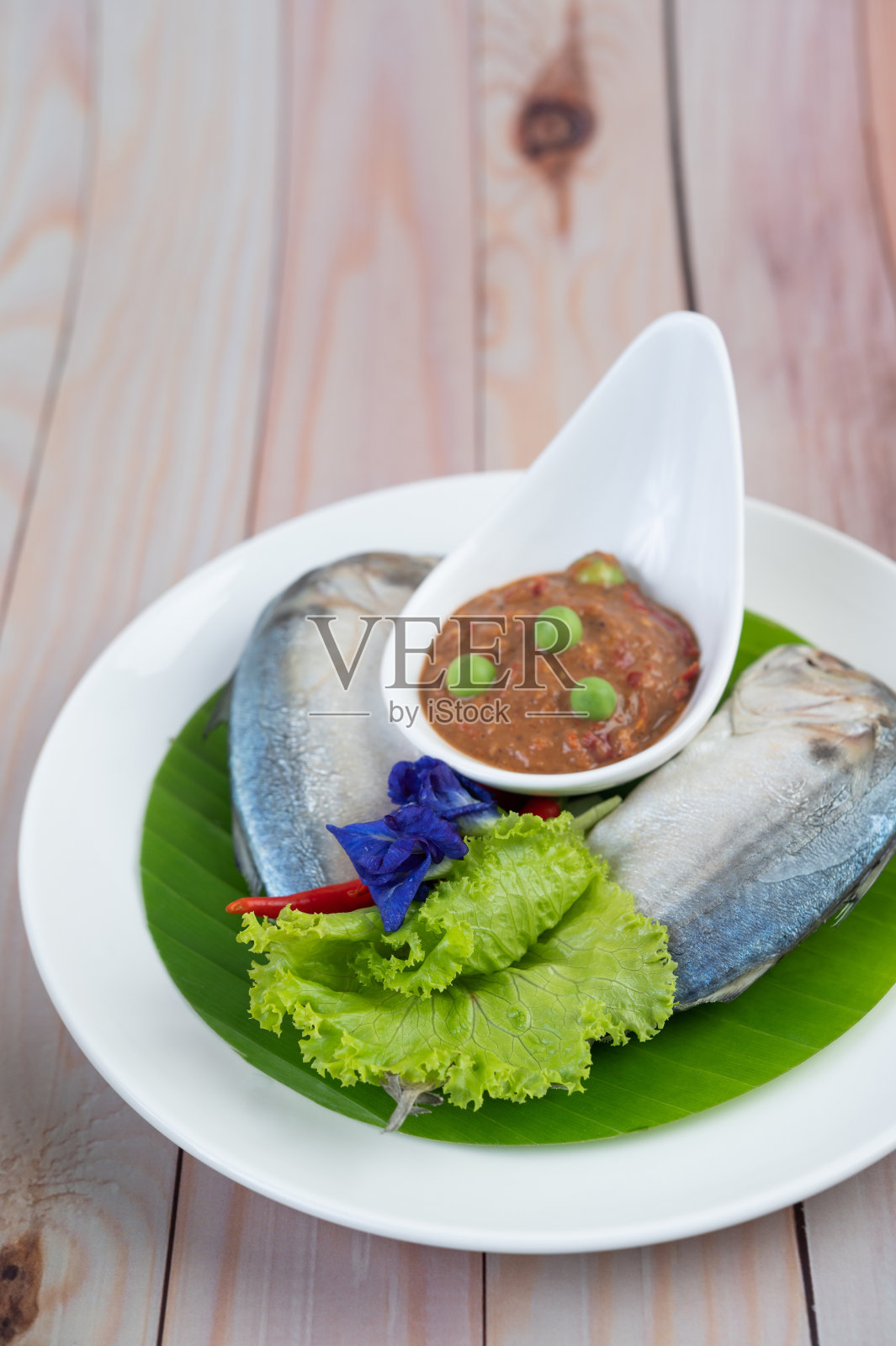 把辣椒酱和鲭鱼放在一个碗里，放一个白盘子和辣椒。沙拉在木地板上照片摄影图片