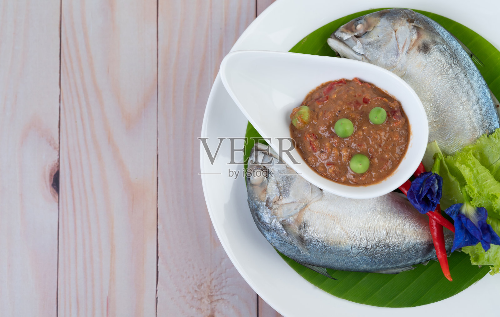 把辣椒酱和鲭鱼放在一个碗里，放一个白盘子和辣椒。沙拉在木地板上照片摄影图片