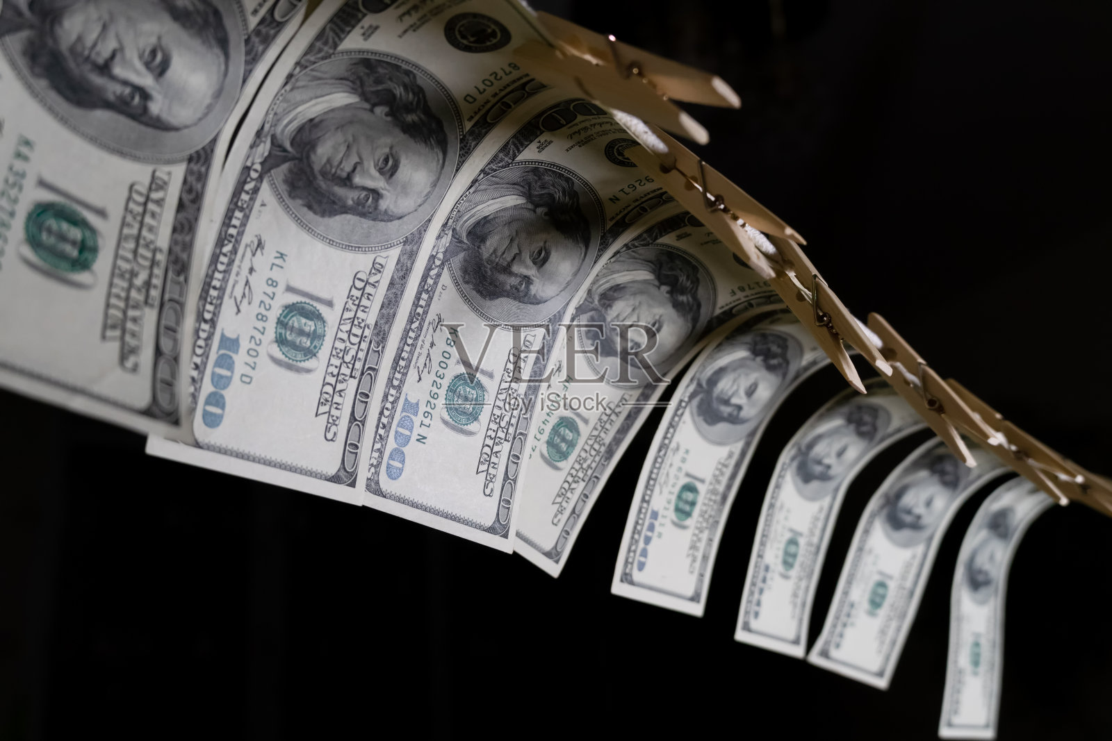 100美元的钞票用一根细绳挂在黑色背景上。脏钱的概念。美元下跌。照片摄影图片