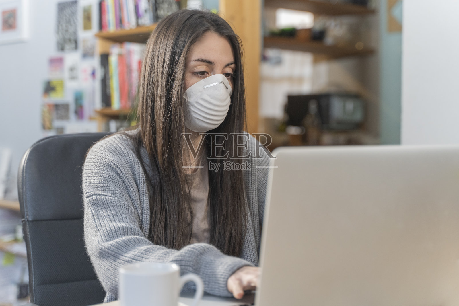 新型冠状病毒：居家办公并佩戴防护口罩的商务女士正在用消毒液清洁双手。照片摄影图片