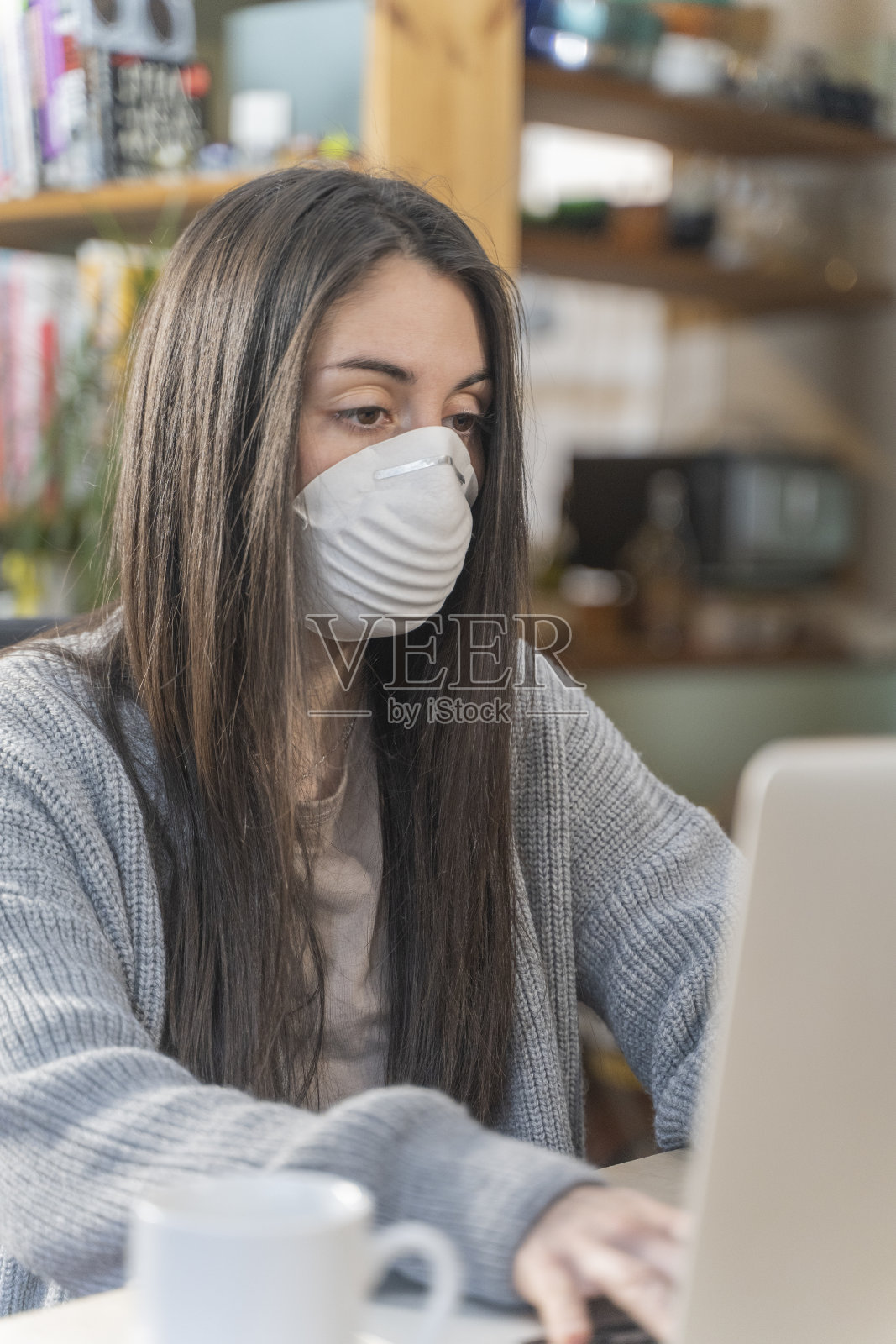 新型冠状病毒：居家办公并佩戴防护口罩的商务女士正在用消毒液清洁双手。照片摄影图片