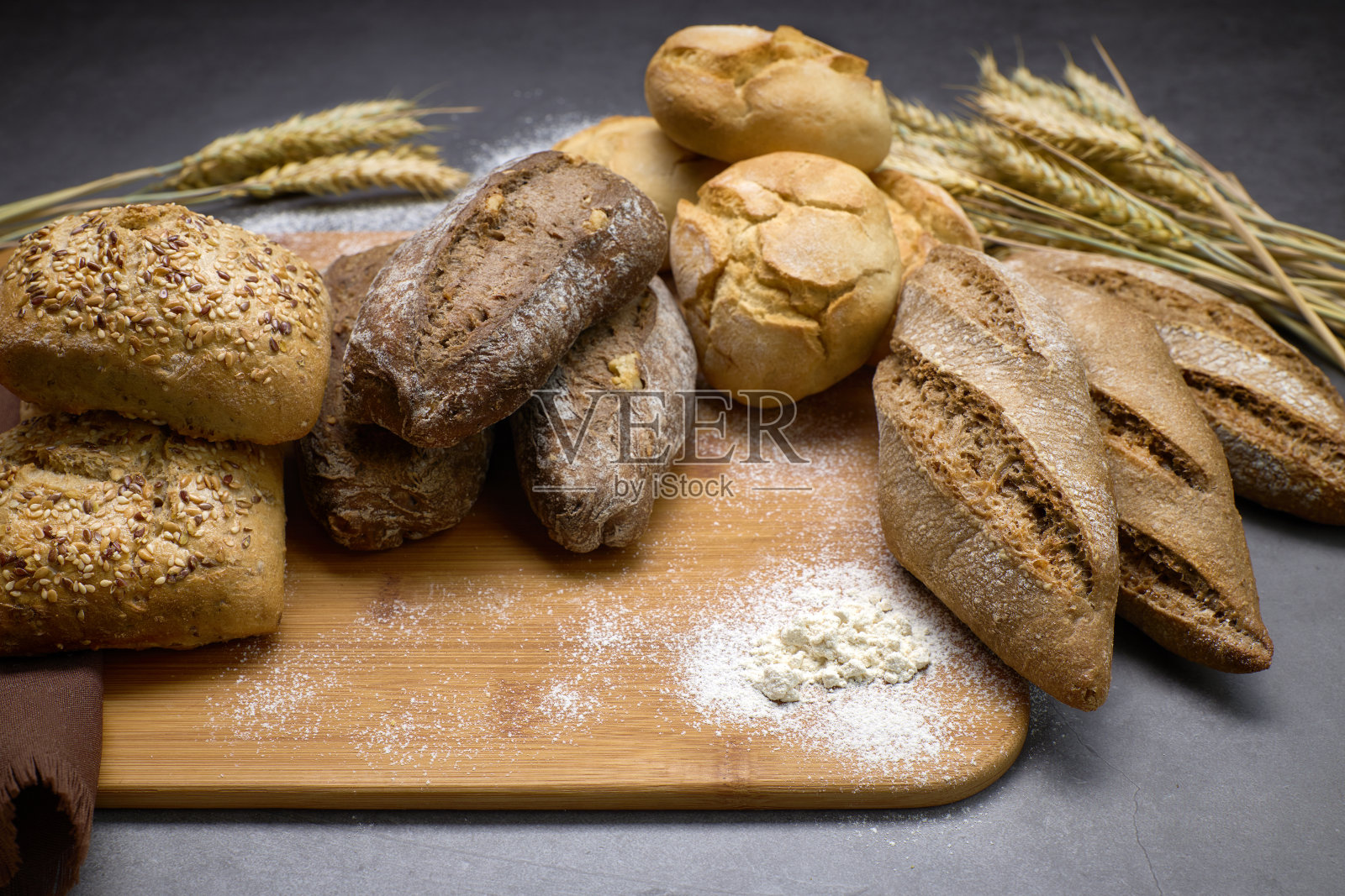 木板上放着美味的面包，旁边是麦穗。照片摄影图片